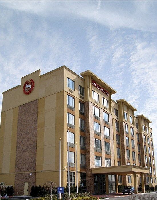 Tall tan hotel building with red signage and a covered entrance under a cloudy sky