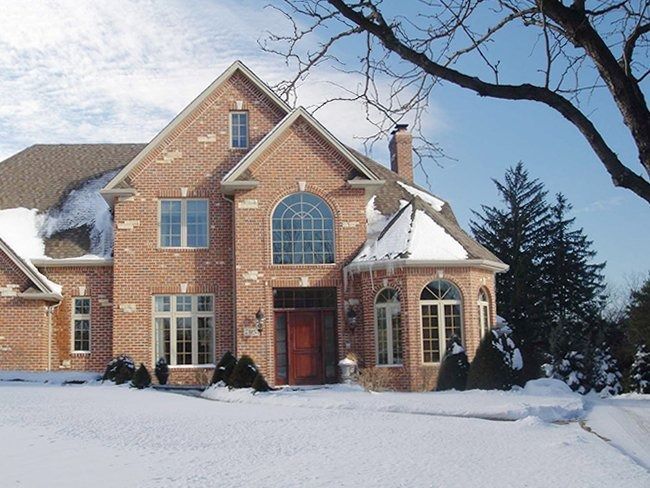 Snow-covered brick house with arched windows and bare trees in winter