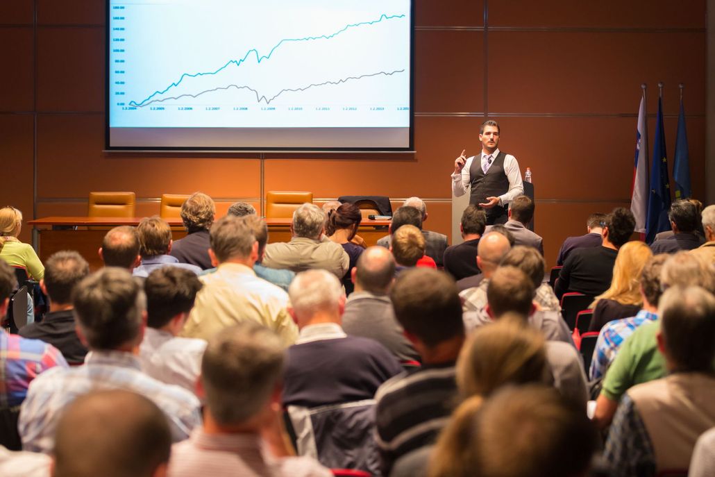 Audience listening to a speaker presenting a chart on a large screen in a conference room