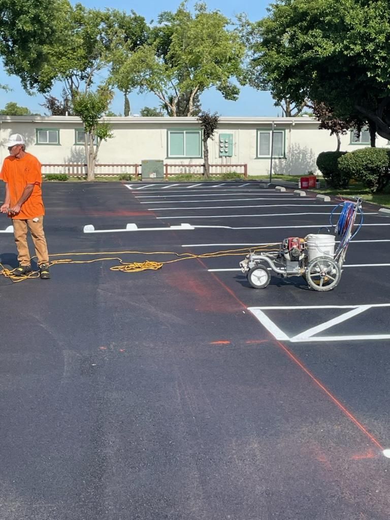 A man in an orange shirt is painting a parking lot