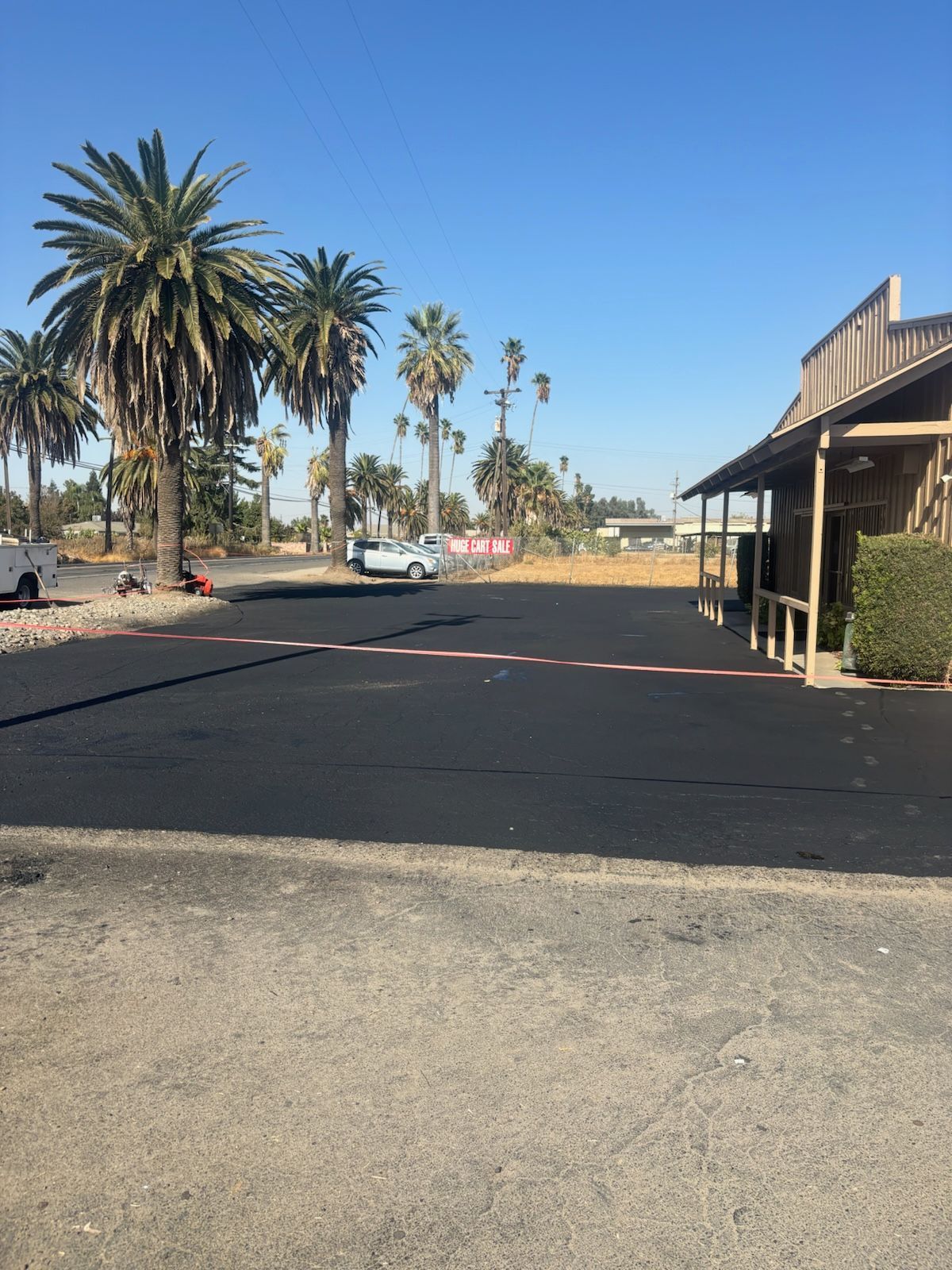 A parking lot with palm trees and a building in the background