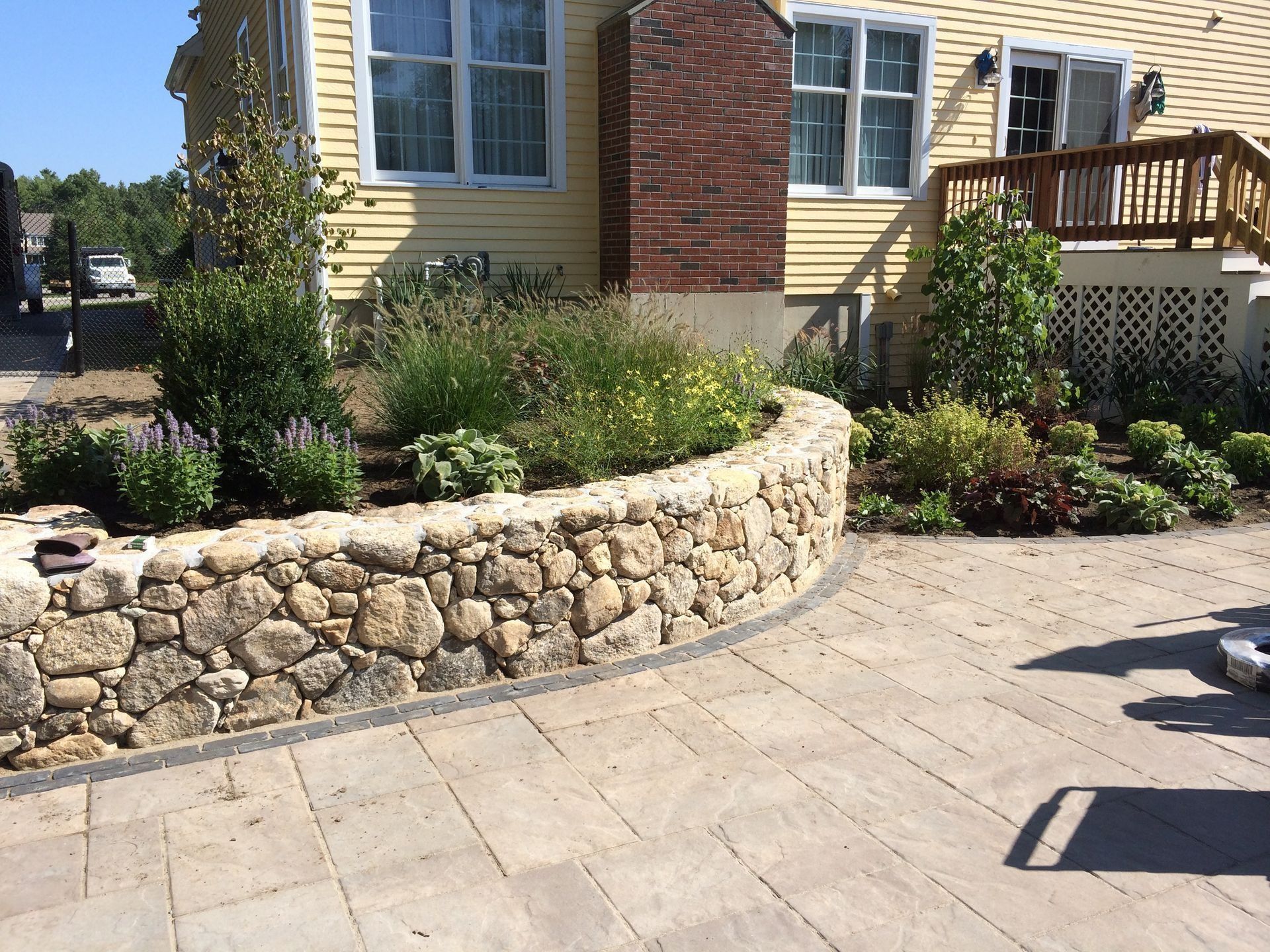 Stone retaining wall with flowerbed, yellow house in background.