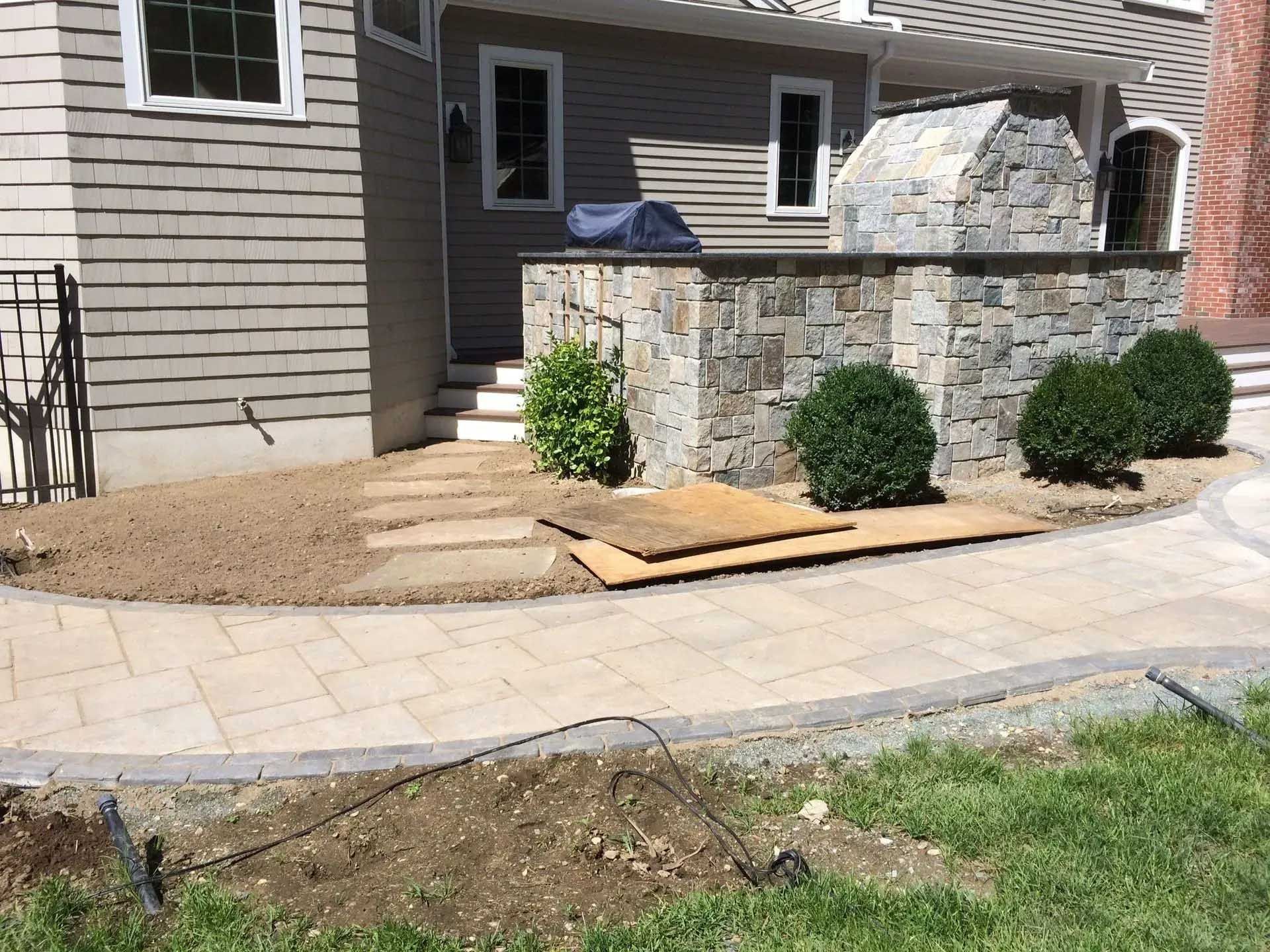 Stone patio with wall and steps leading to a house entrance, with landscaping and green grass.