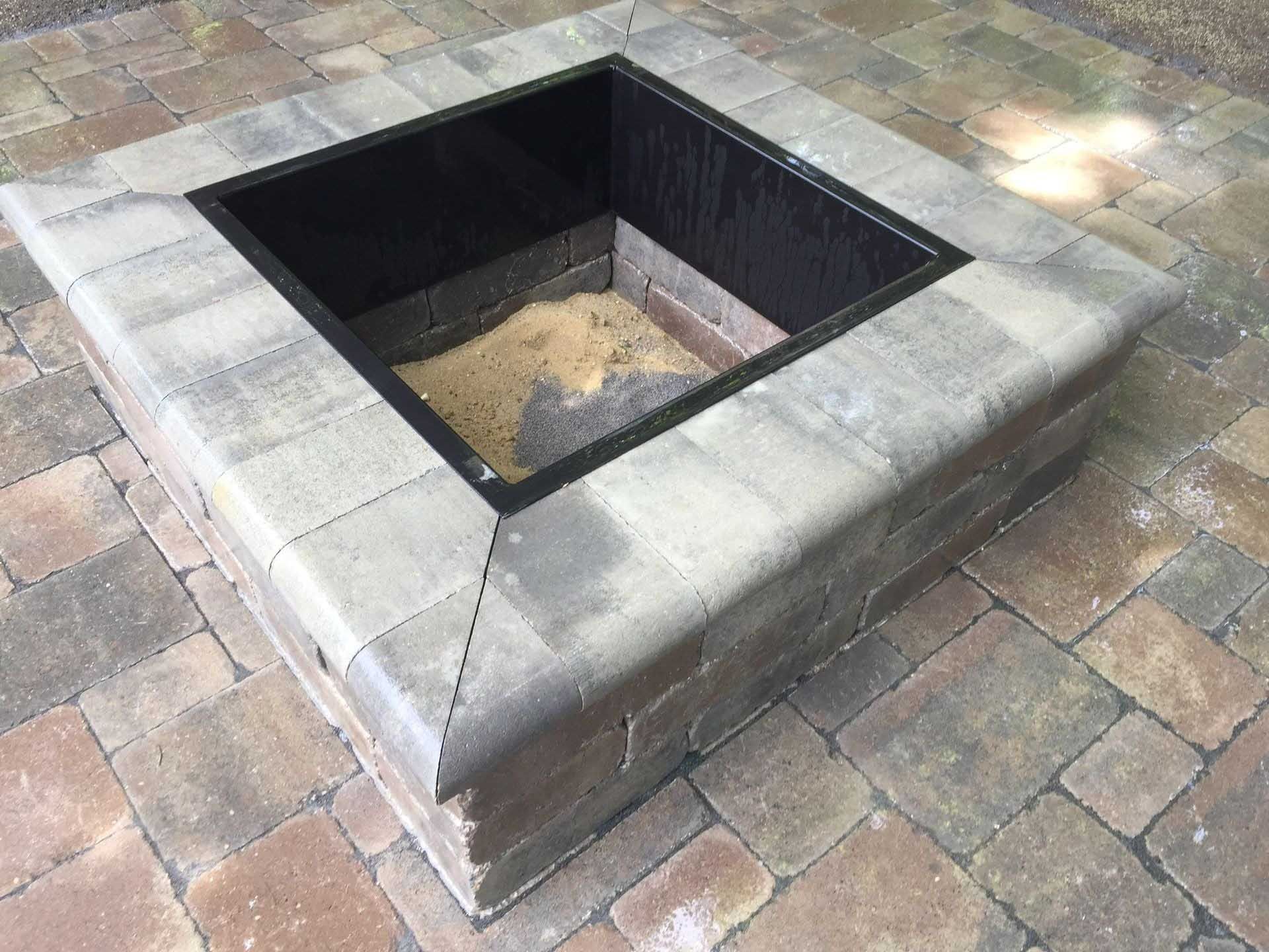 Stone fire pit with a dark metal insert on a brick patio.