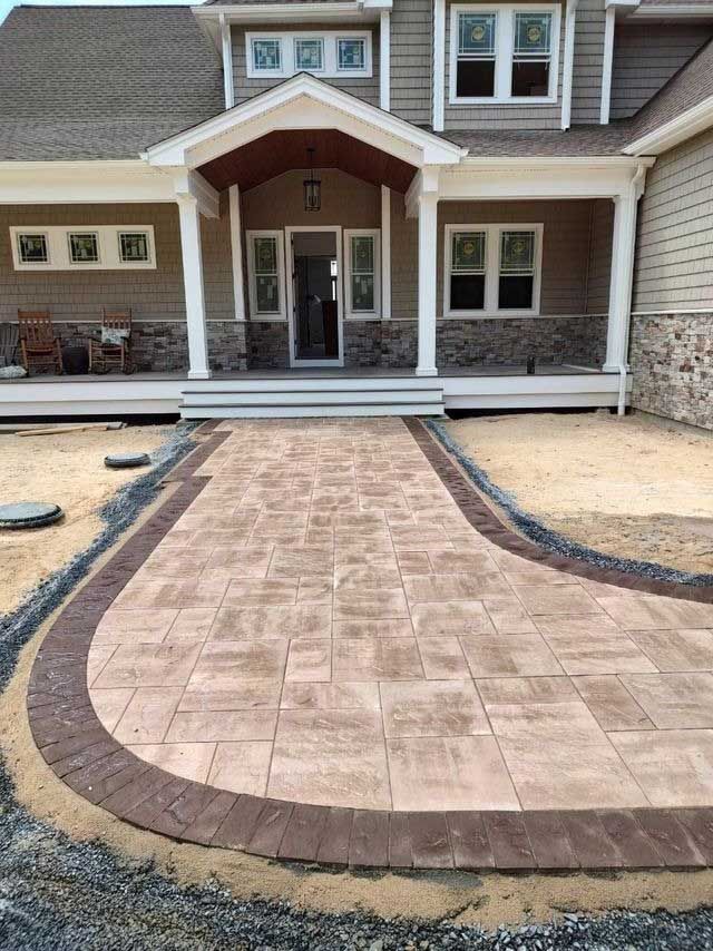 Brick pathway leads to a house entrance with columns. Light and dark brick are used.