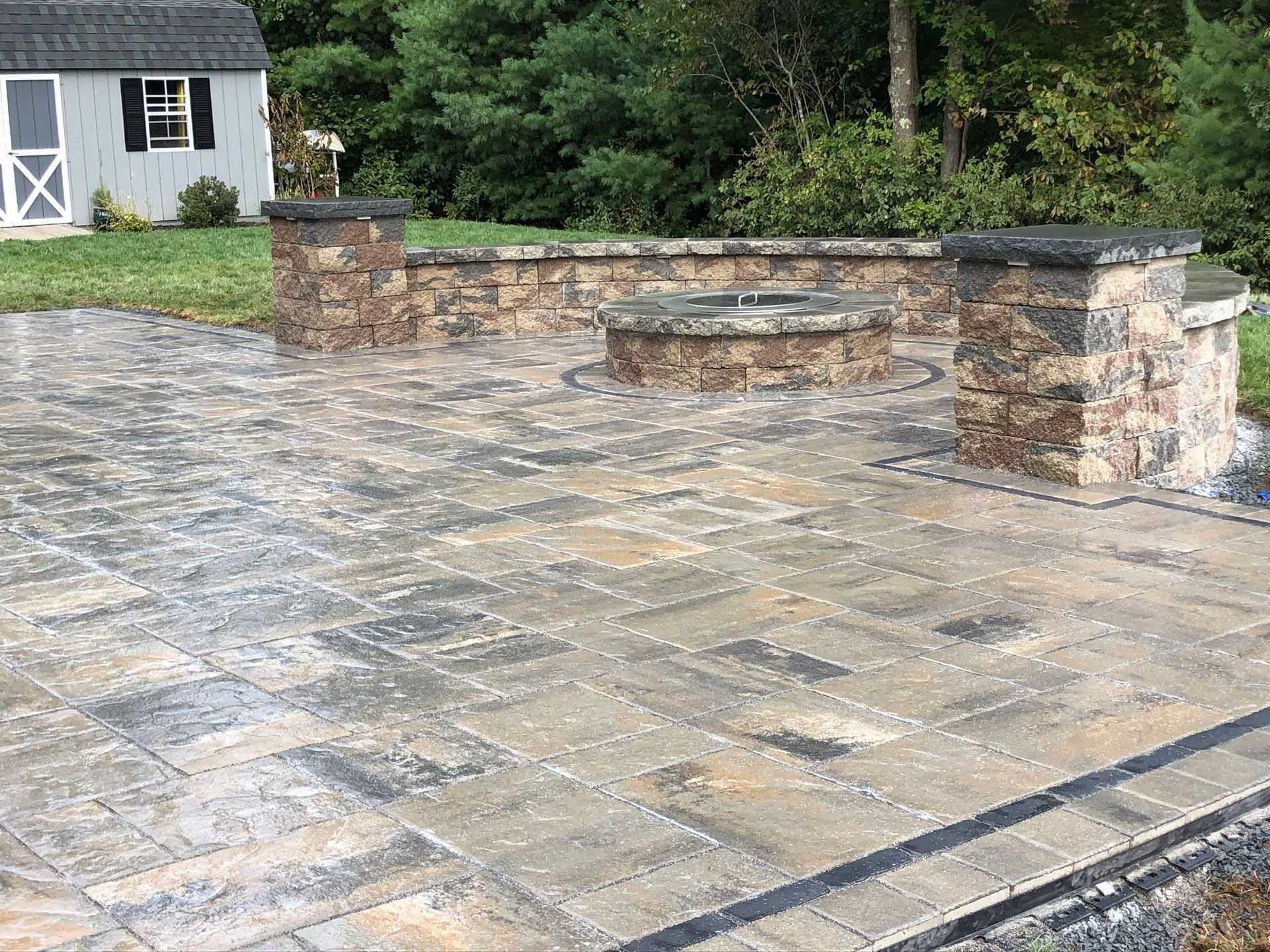 Stone patio with fire pit and low wall, backyard setting.