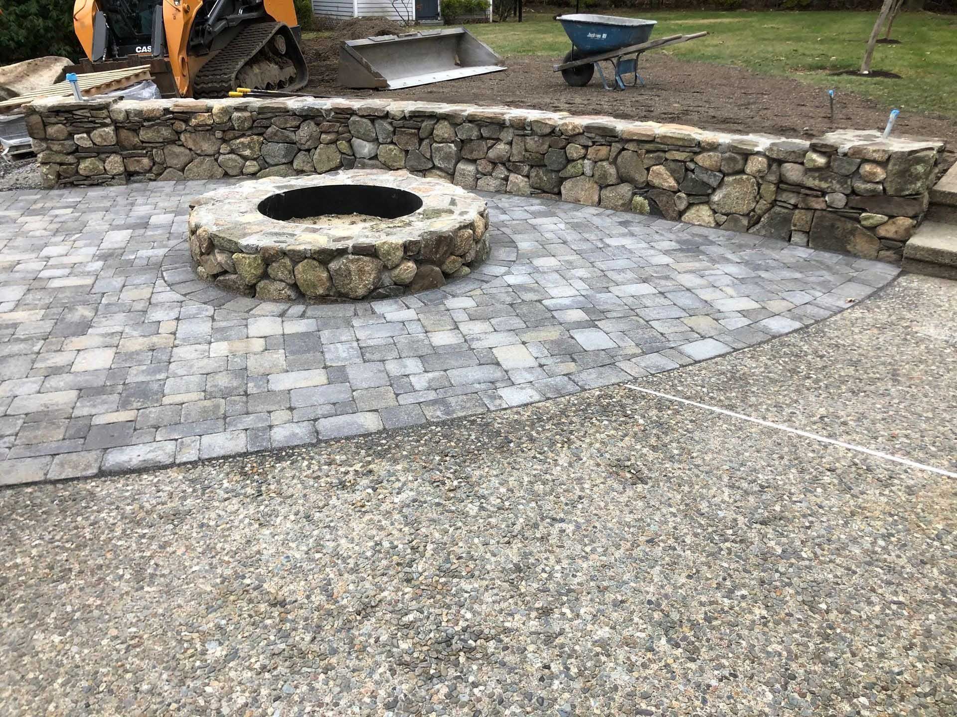 Stone patio with fire pit, surrounded by a stone wall and gravel path.