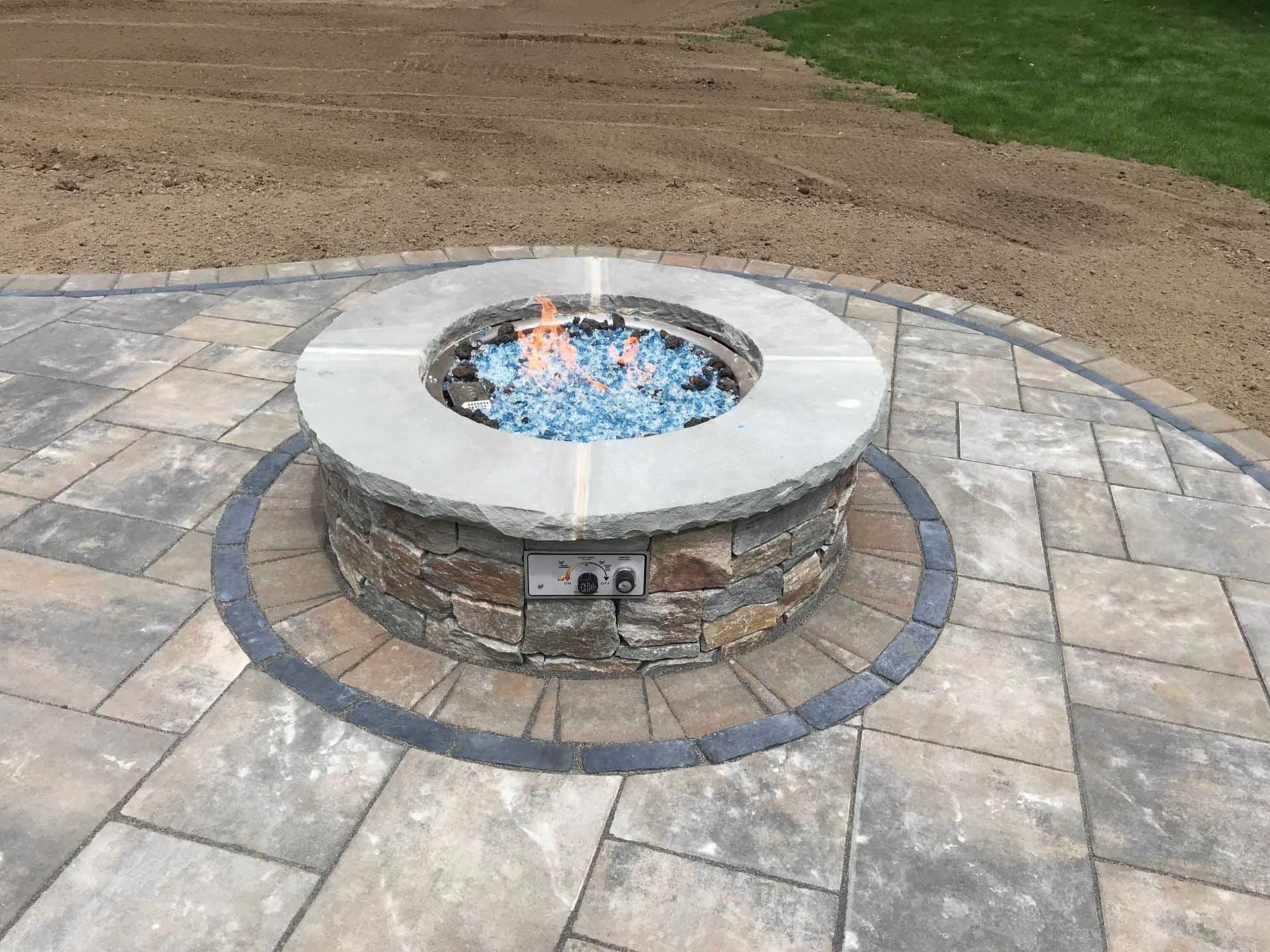 Fire pit with blue glass rocks on a stone patio.
