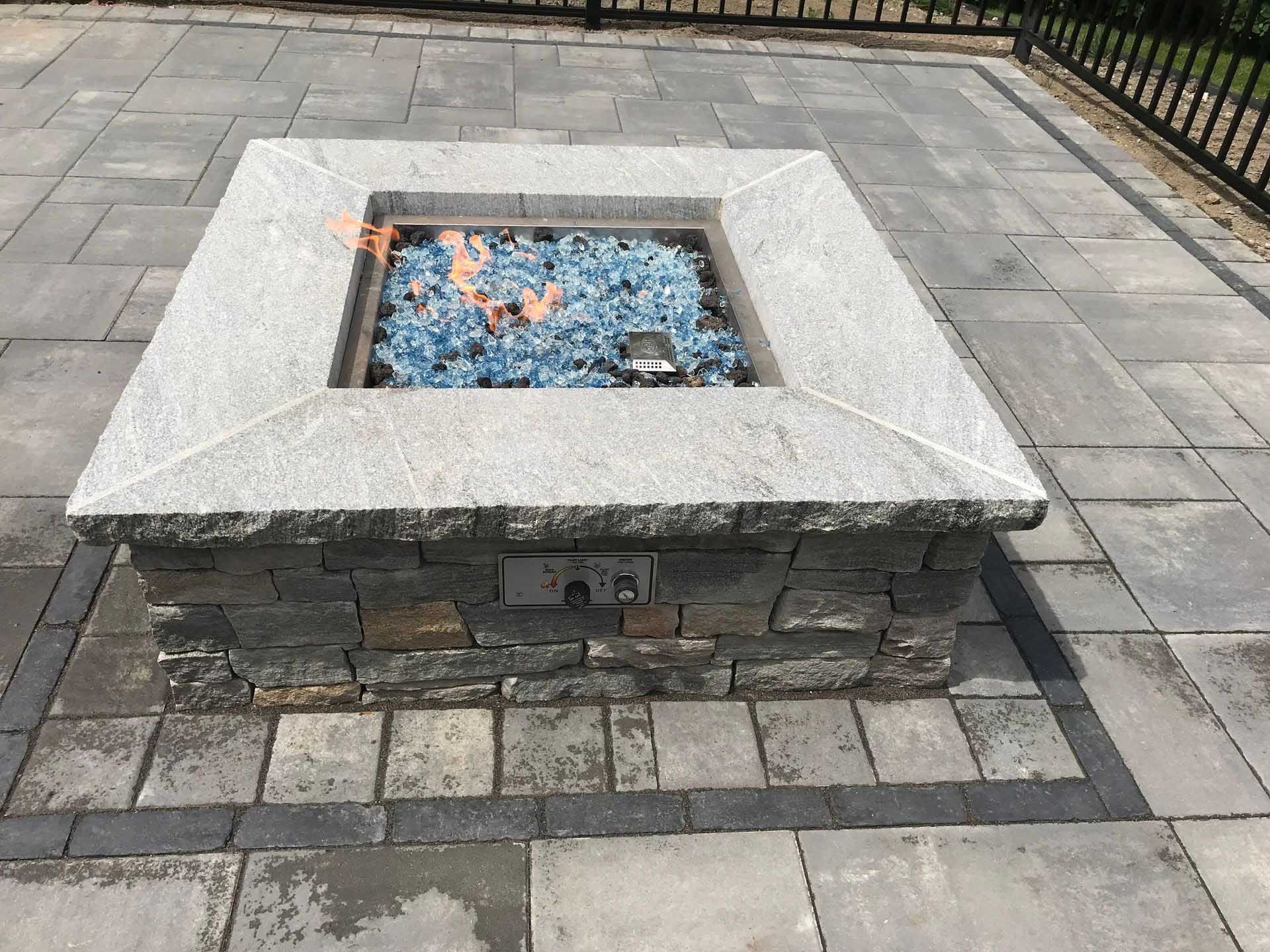 Fire pit with blue glass and flames on stone patio.