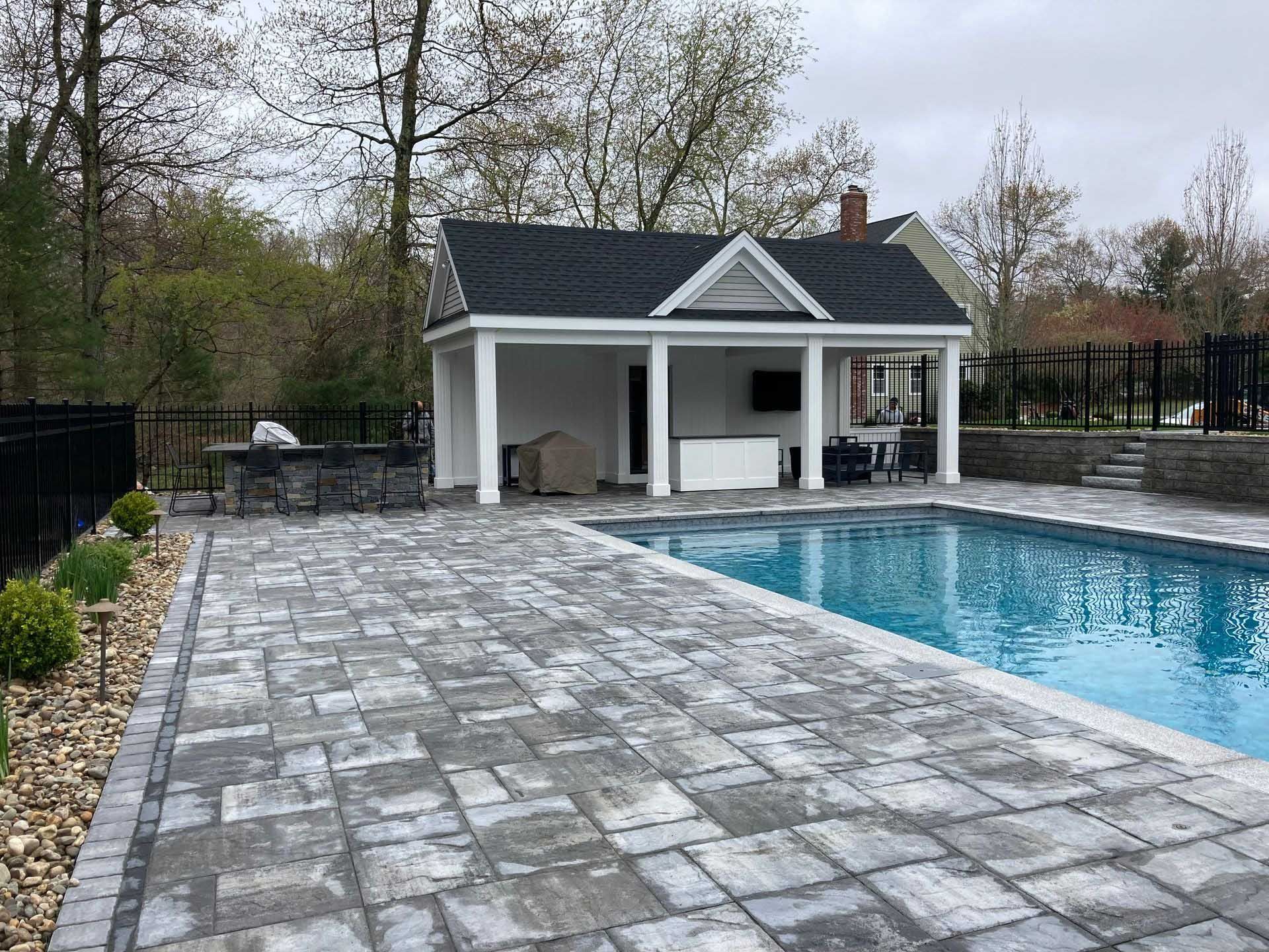 Pool area with a stone patio, pool house, and a pool.