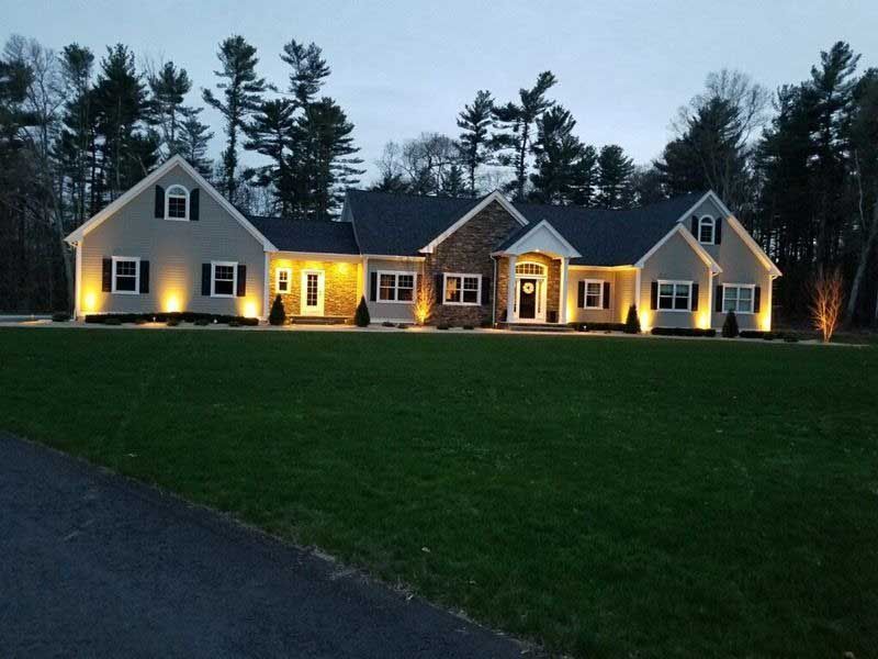 A well-lit beige ranch-style house with a stone facade and large front lawn, at dusk.