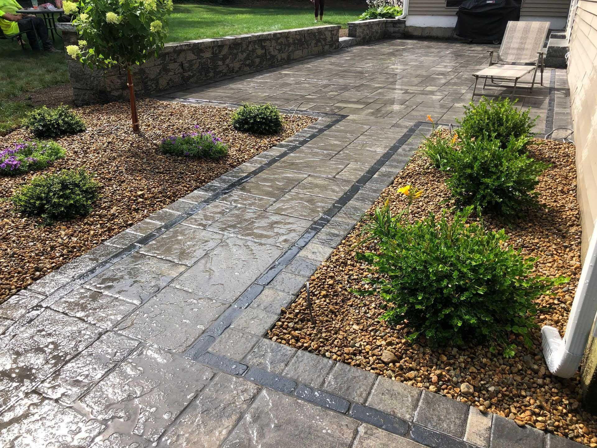 Stone patio with gravel borders, small shrubs, and a retaining wall.