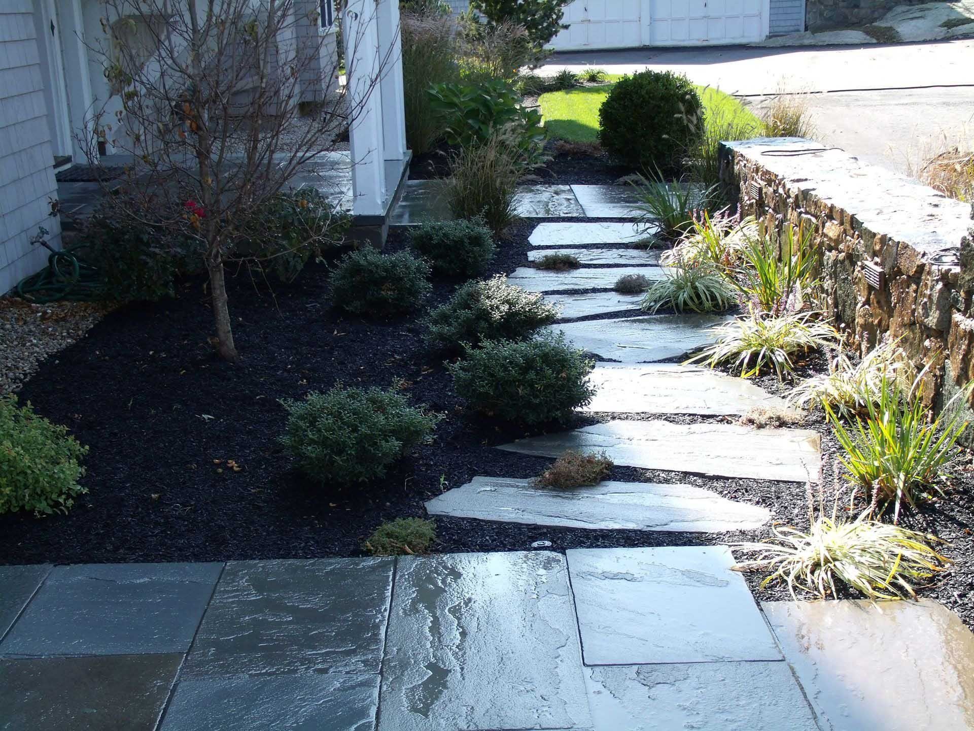 Stone pathway through landscaped garden with shrubs and mulch.
