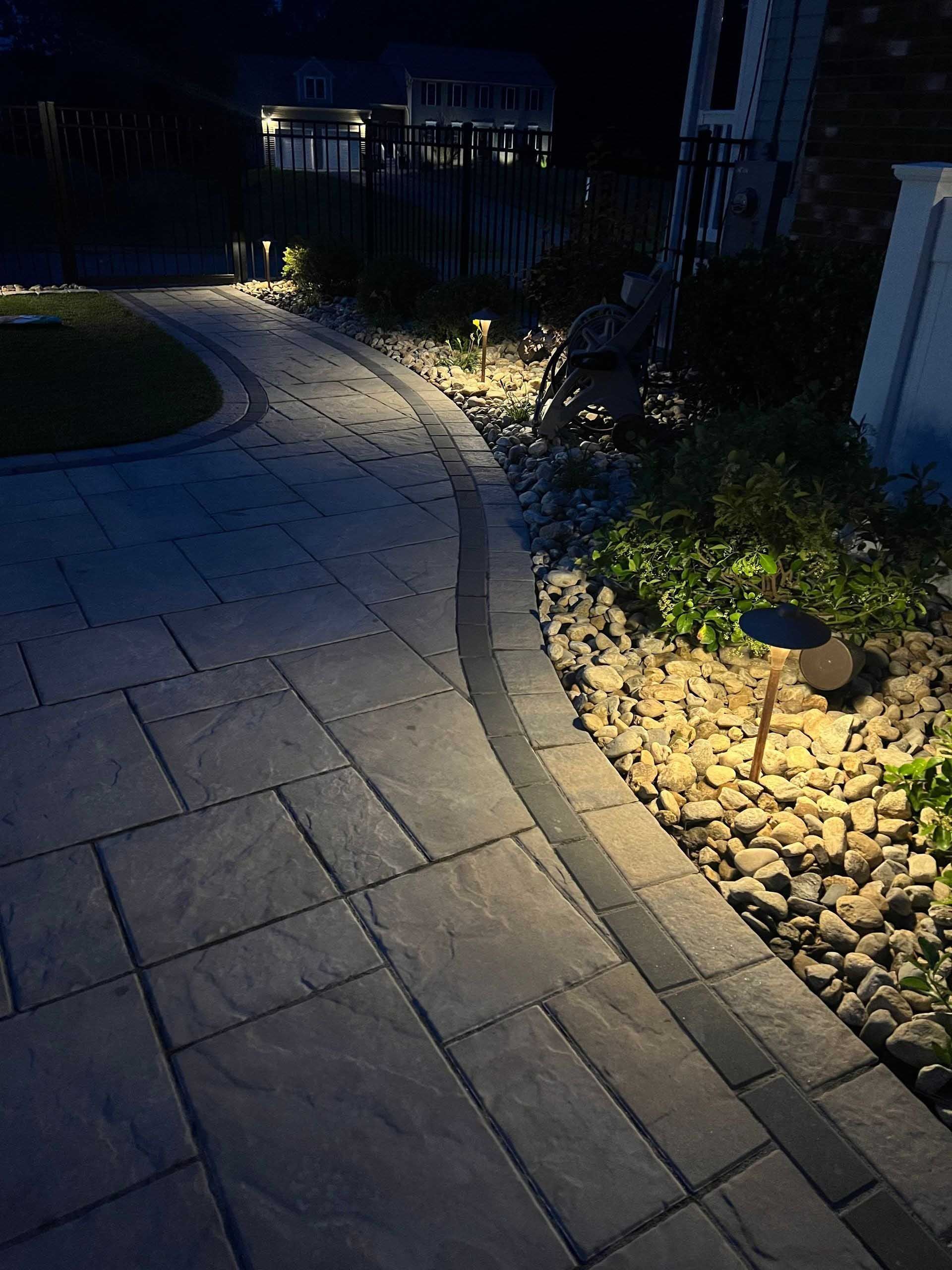 Lit stone pathway curves at night with garden lights and landscaping.