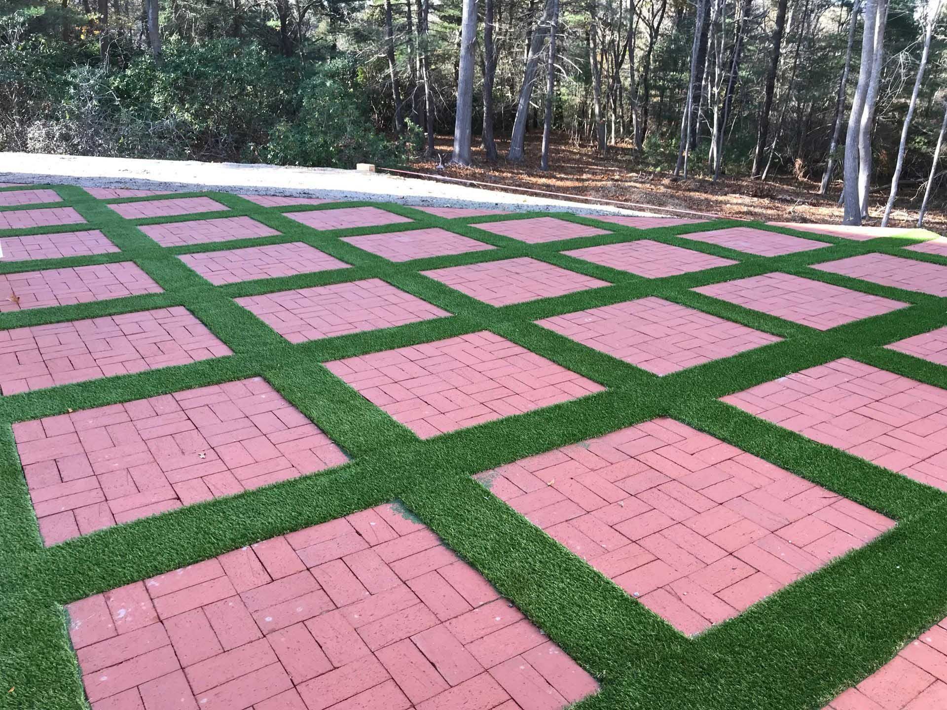 Brick pavers arranged in squares with artificial turf between them, outdoor setting.