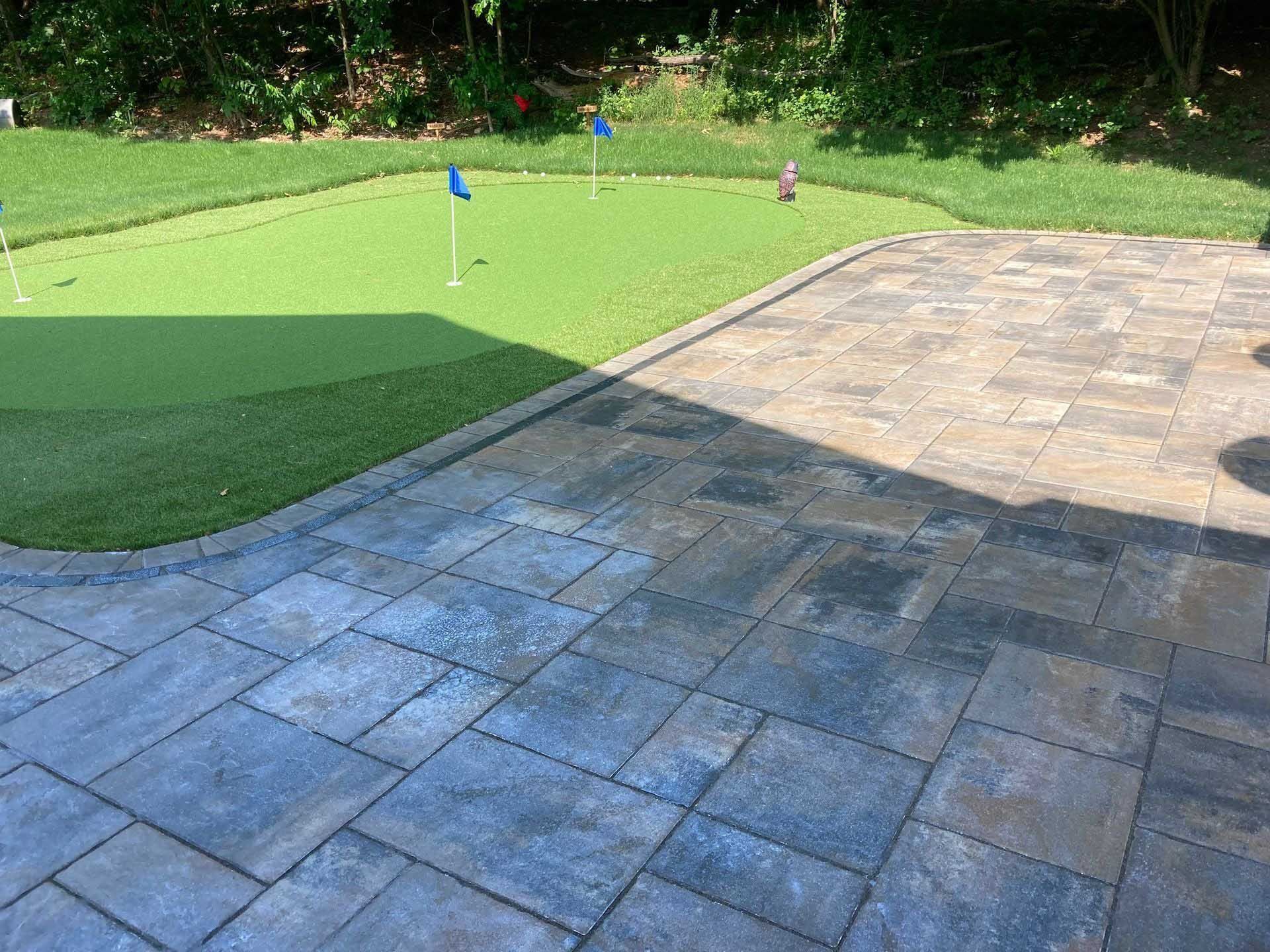 Patio with gray pavers next to a putting green with blue flags.