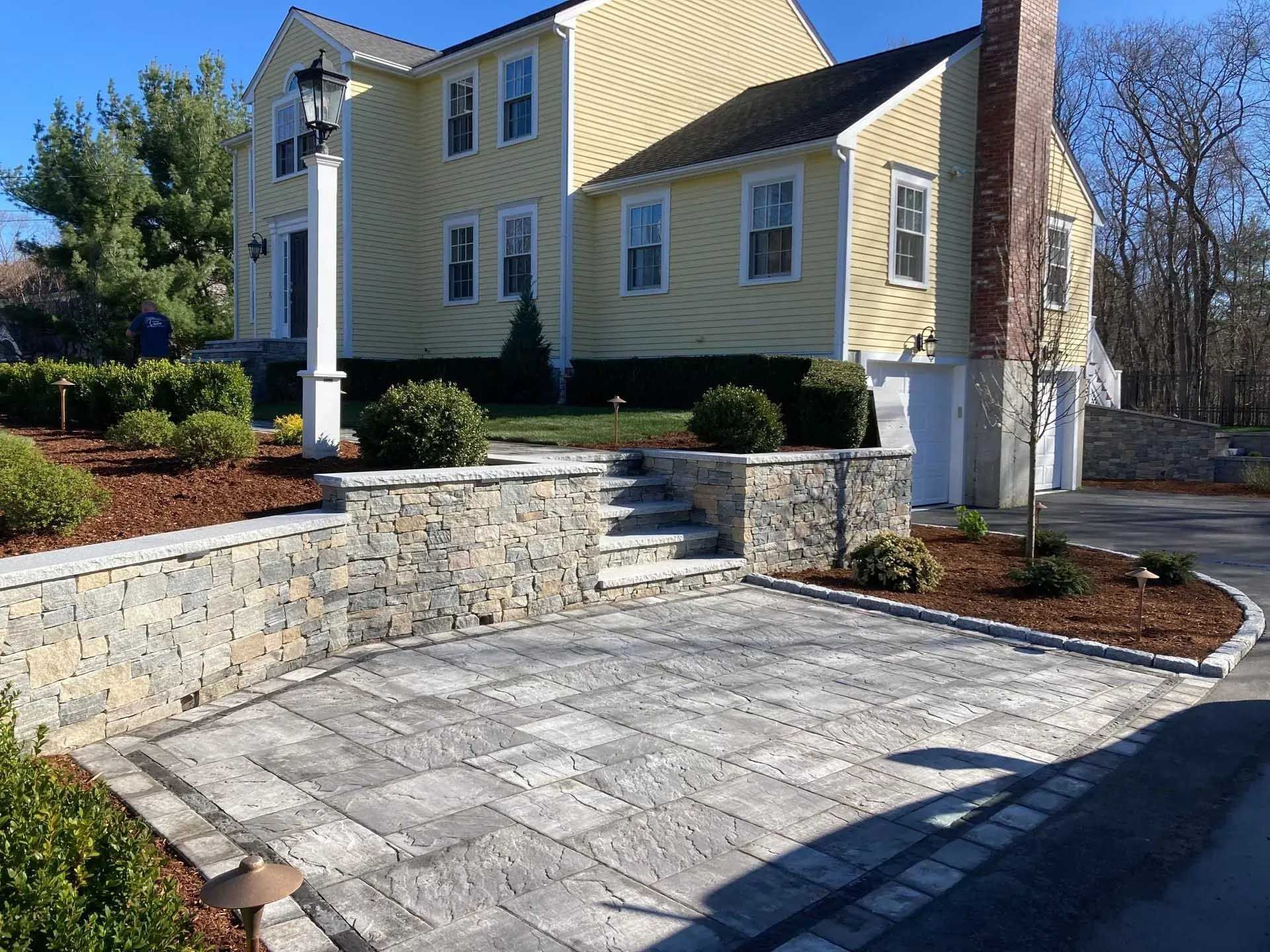 Yellow house with stone retaining walls, steps, and a paved driveway.