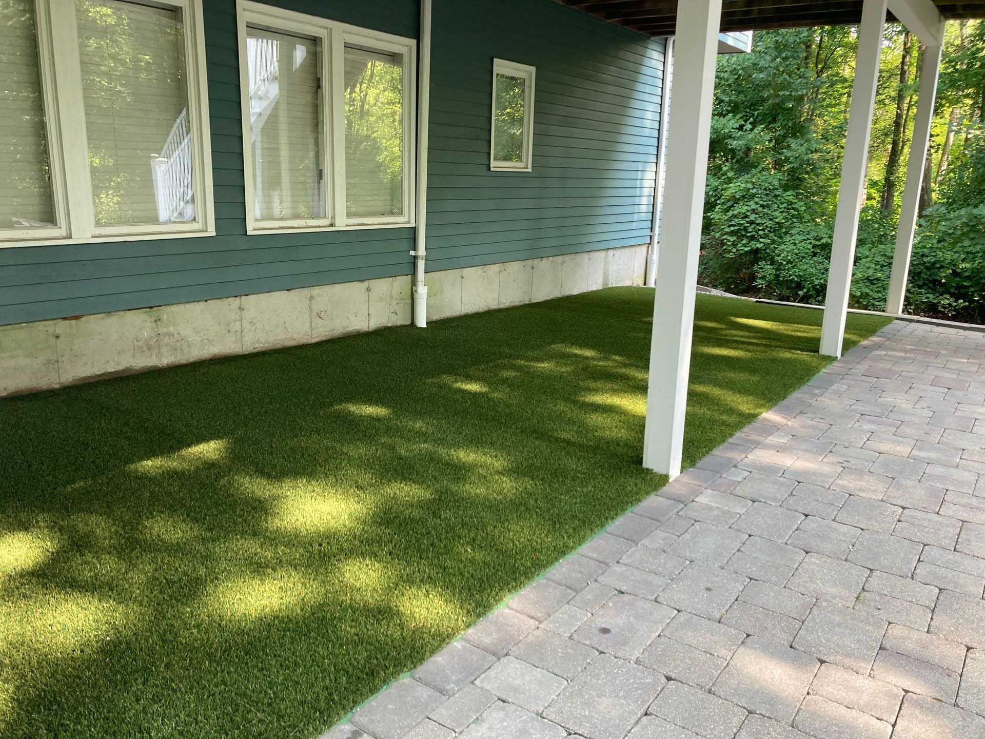 Green artificial turf beside a brick patio, under a blue building with white trim.