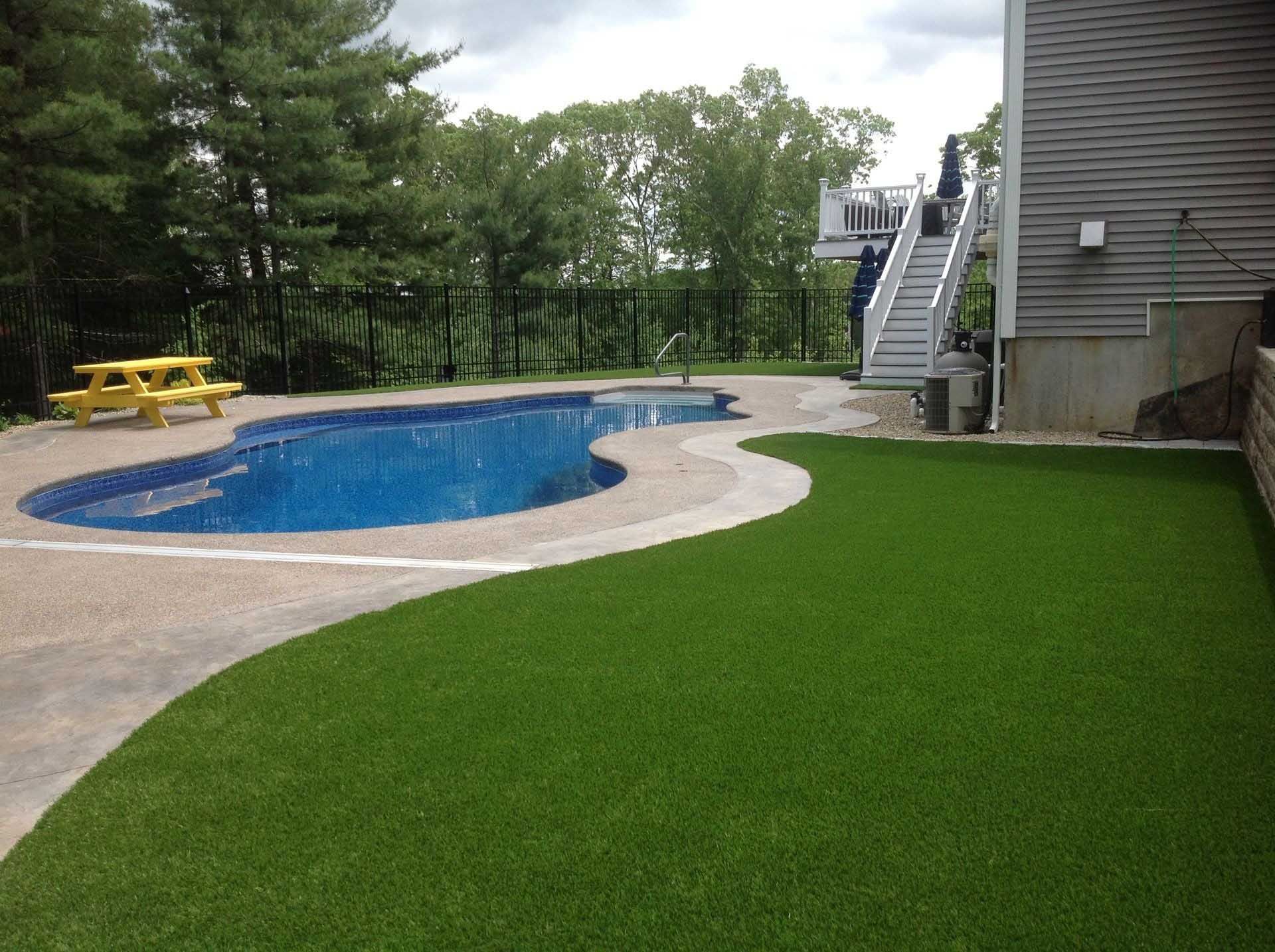 A backyard with a blue pool, green lawn, and a wooden picnic table; a house is to the right.