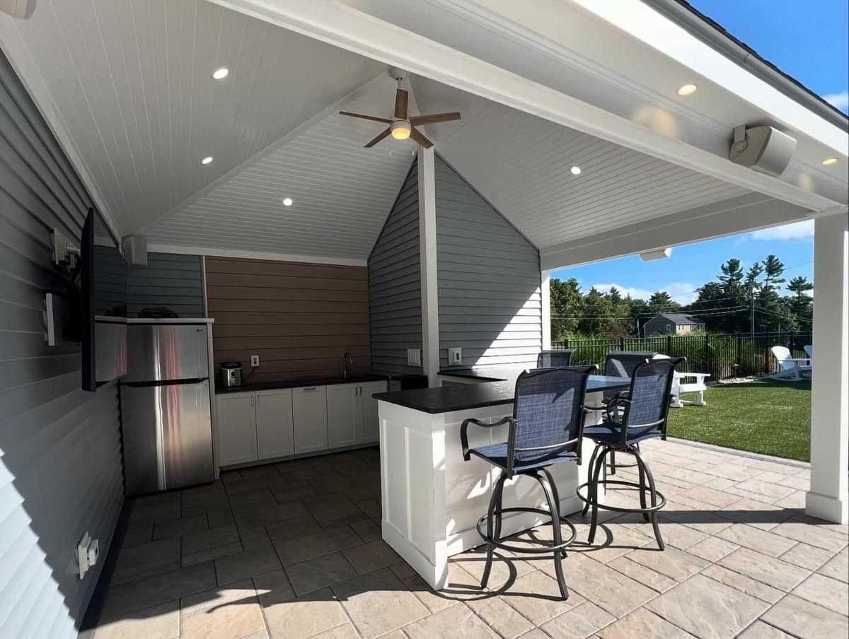 Outdoor kitchen with a bar, fridge, TV, and seating under a covered patio.