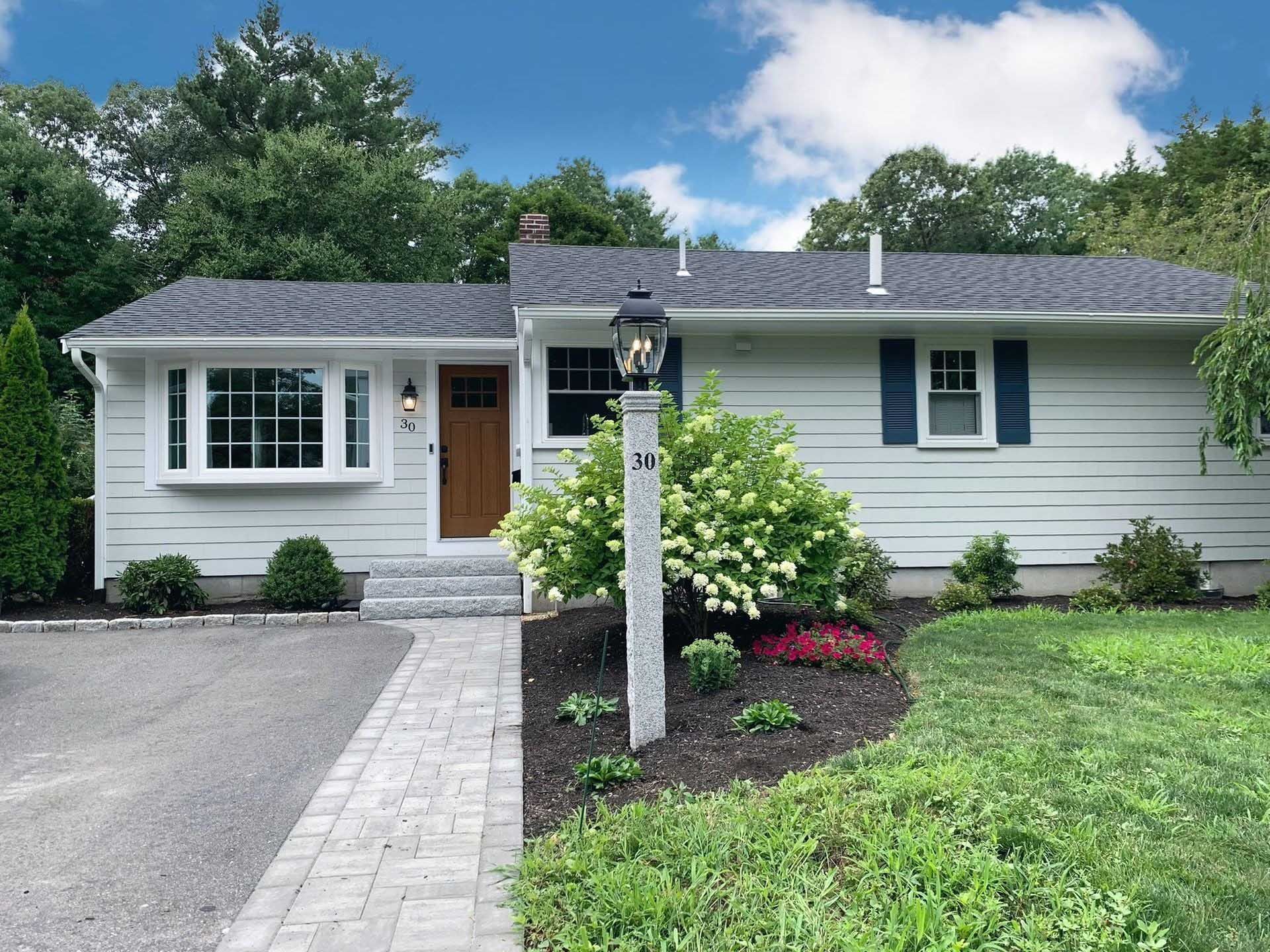 White ranch house with bay window, blue shutters, brick path, and landscaped yard.
