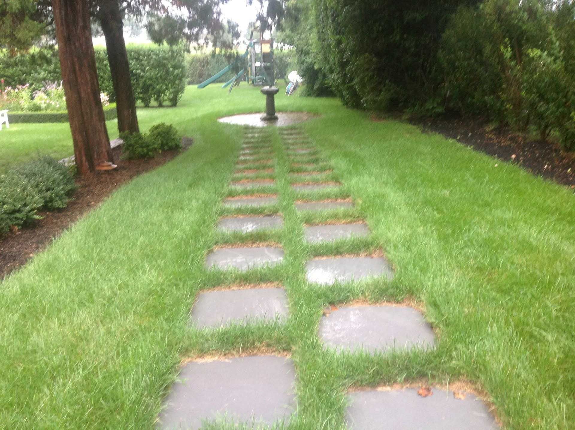 Stone pathway through green lawn, leading to a water fountain.