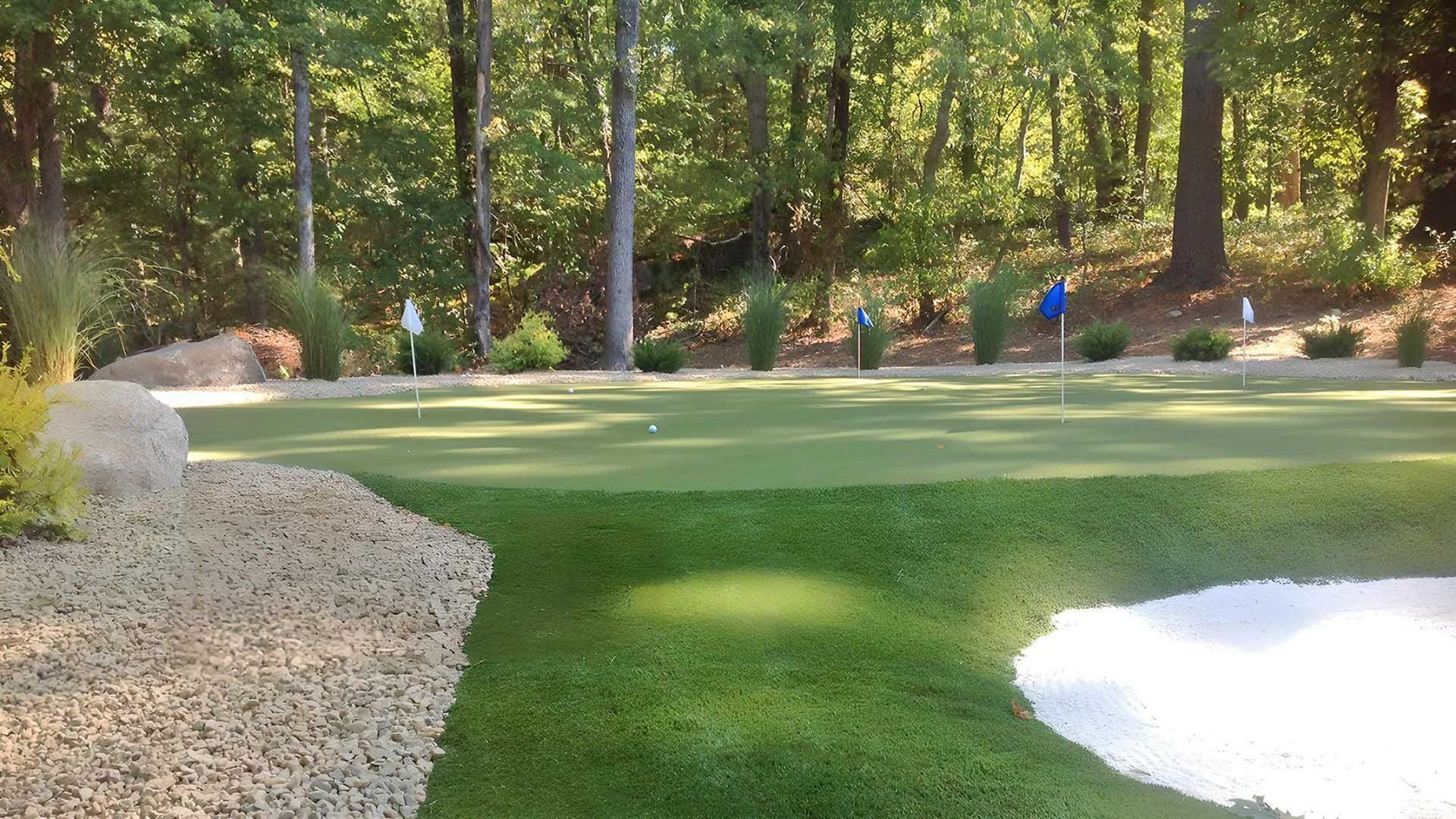A golf green with a sand trap, trees, and a flag.