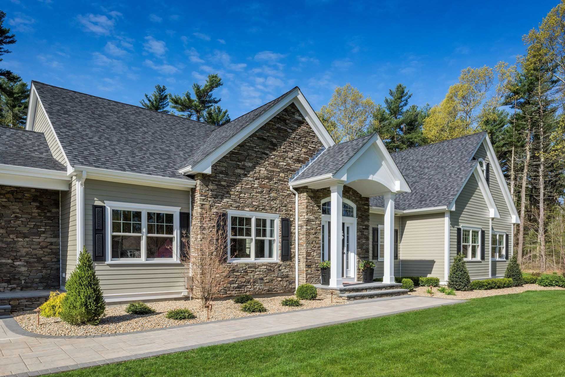 House with stone and siding exterior, surrounded by a green lawn and trees under a blue sky.