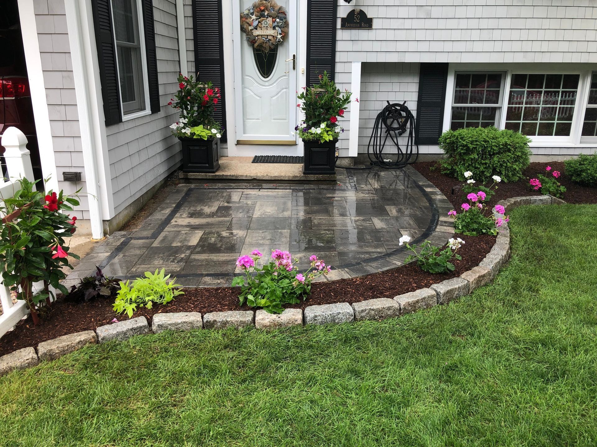 Front porch with a gray stone patio, flowers, and potted plants.