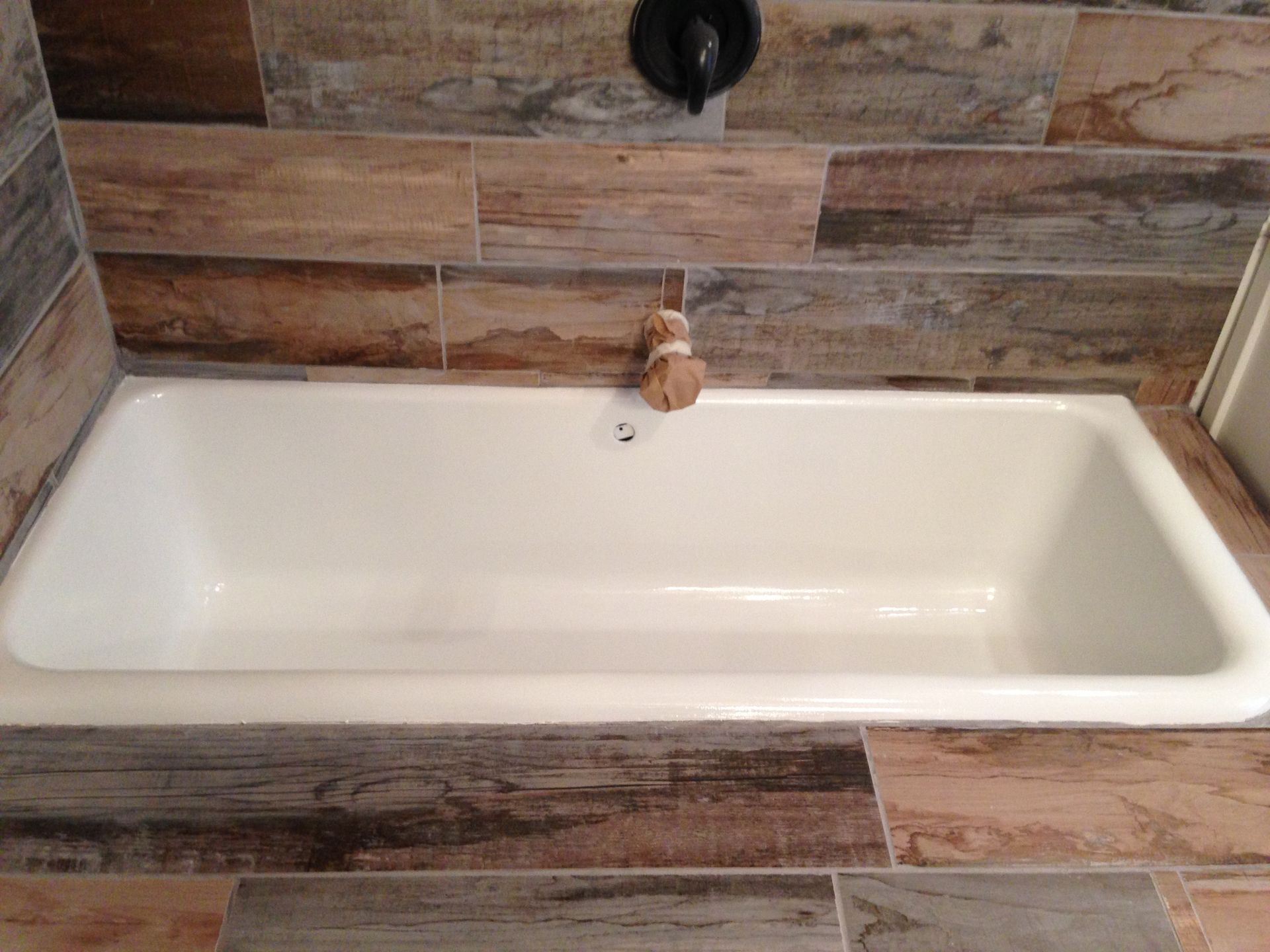 A bathtub in a bathroom with wooden tiles and a faucet - after