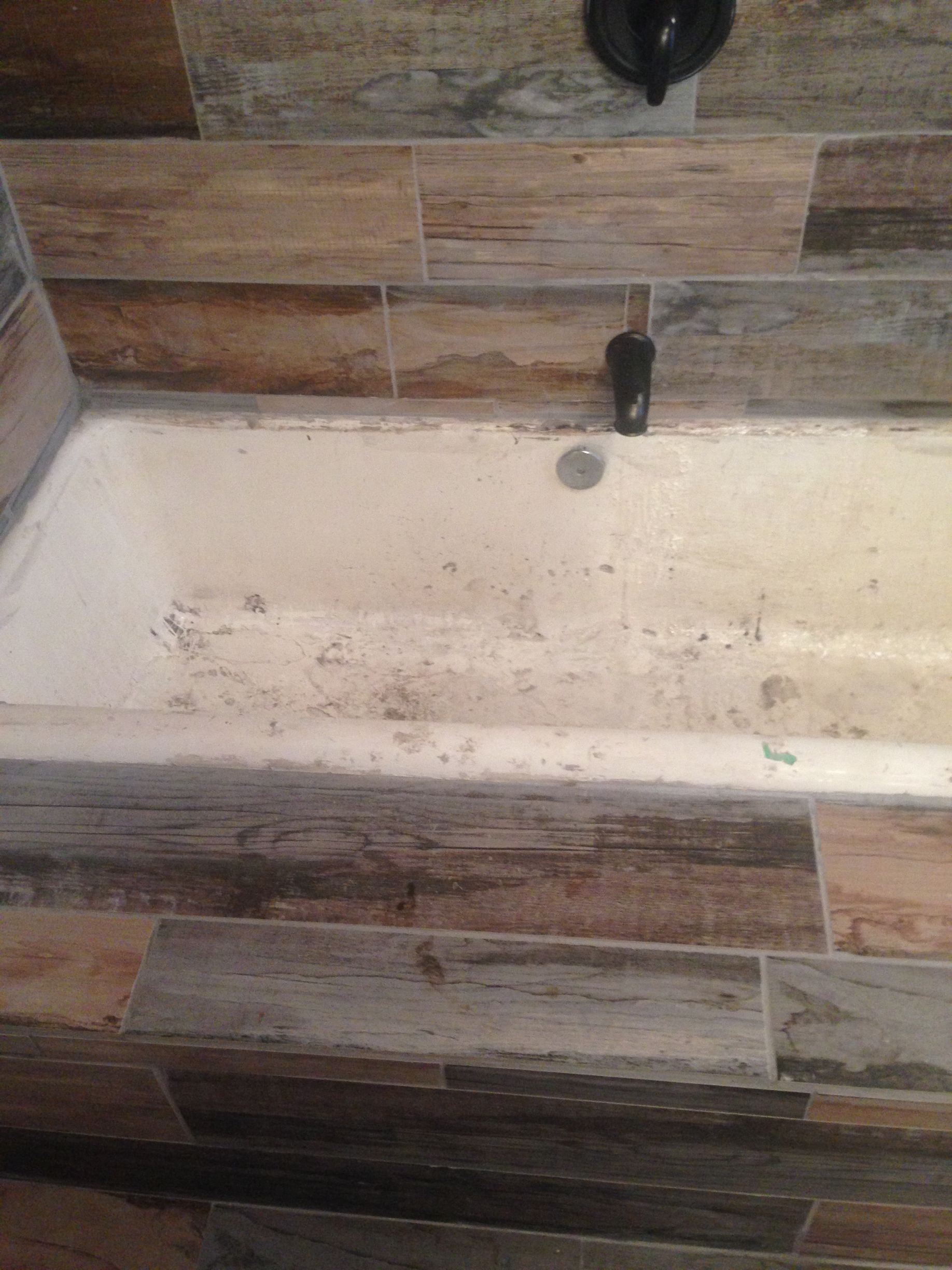 A bathtub in a bathroom with wooden tiles and a faucet - before