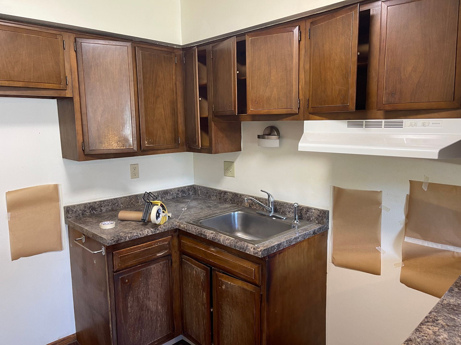 A kitchen with wooden cabinets and a stainless steel sink - before