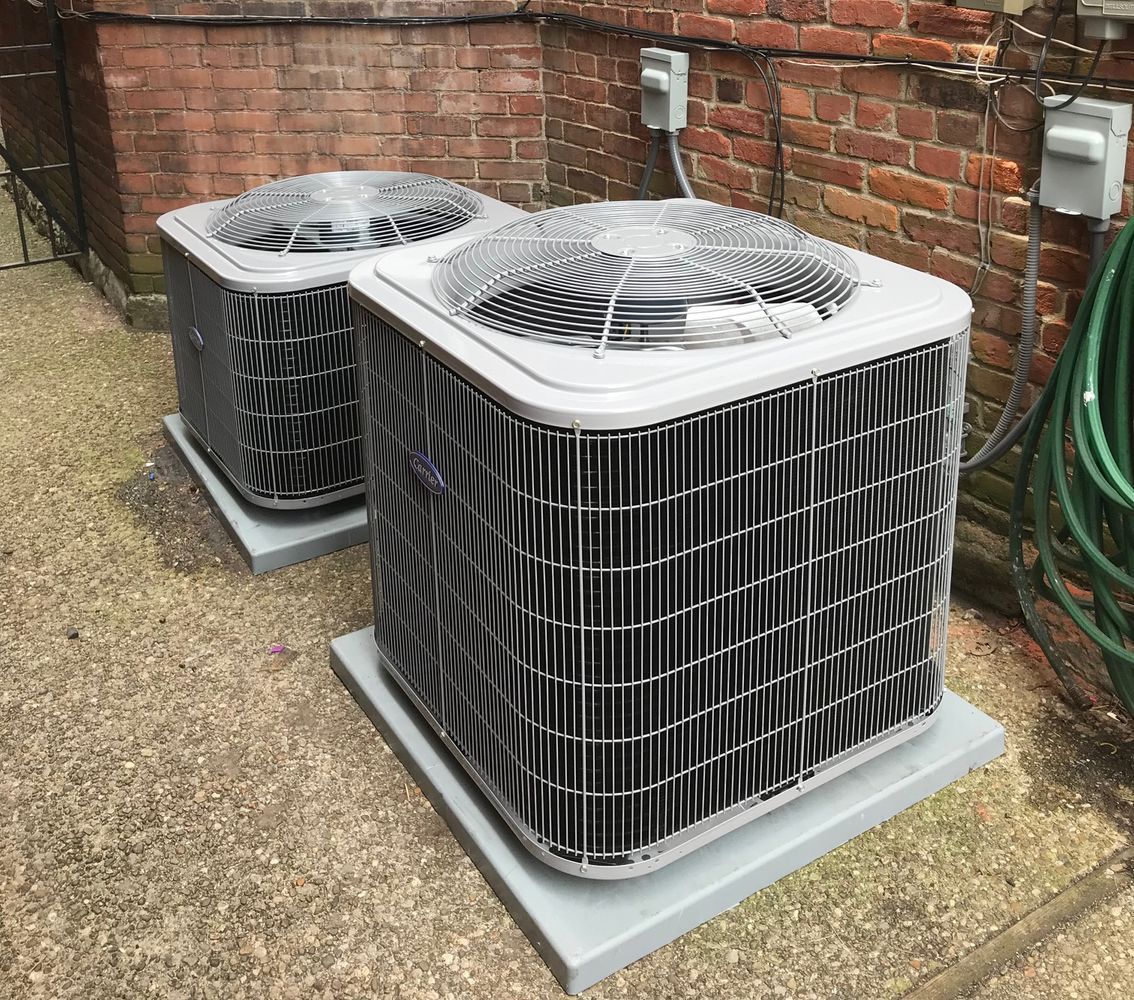 Two air conditioners are sitting on the side of a brick building.