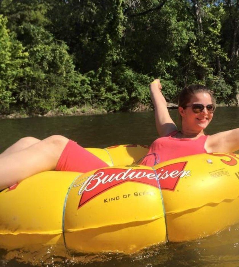 A woman is laying on a budweiser tube in the water