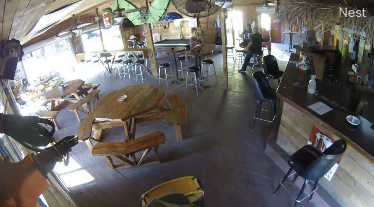 A man is standing in a restaurant with tables and chairs.