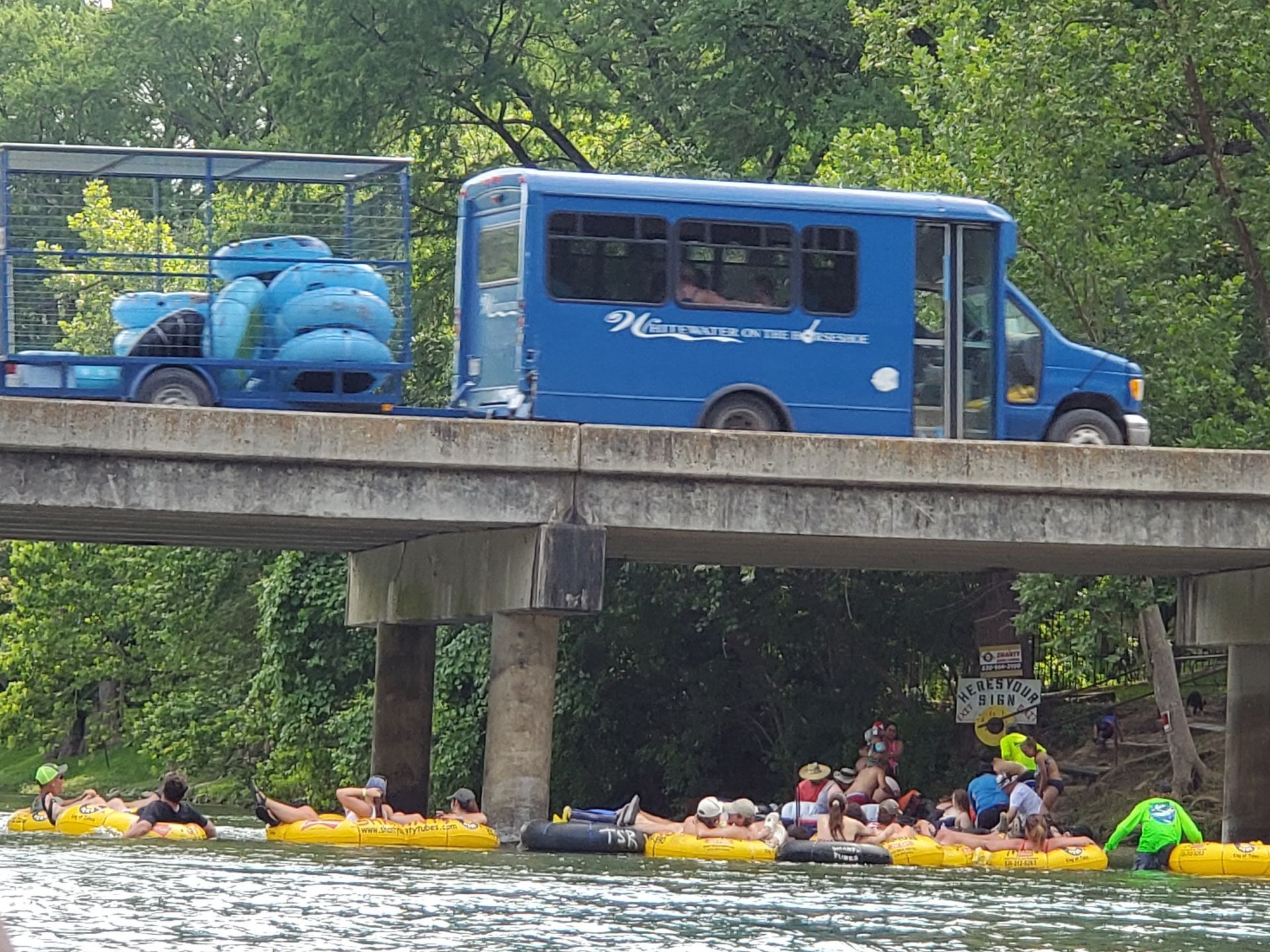 A blue bus is driving over a bridge over a river