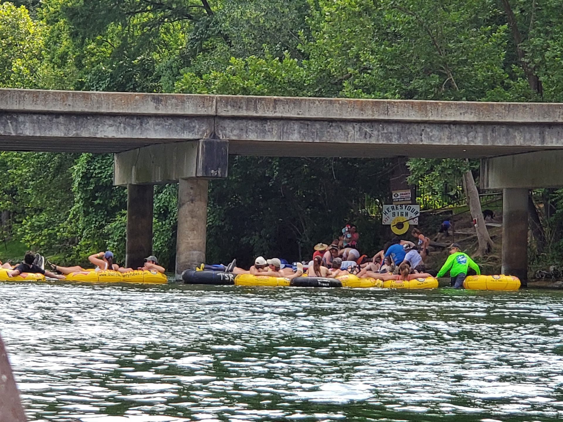 A group of people are tubing down a river under a bridge.
