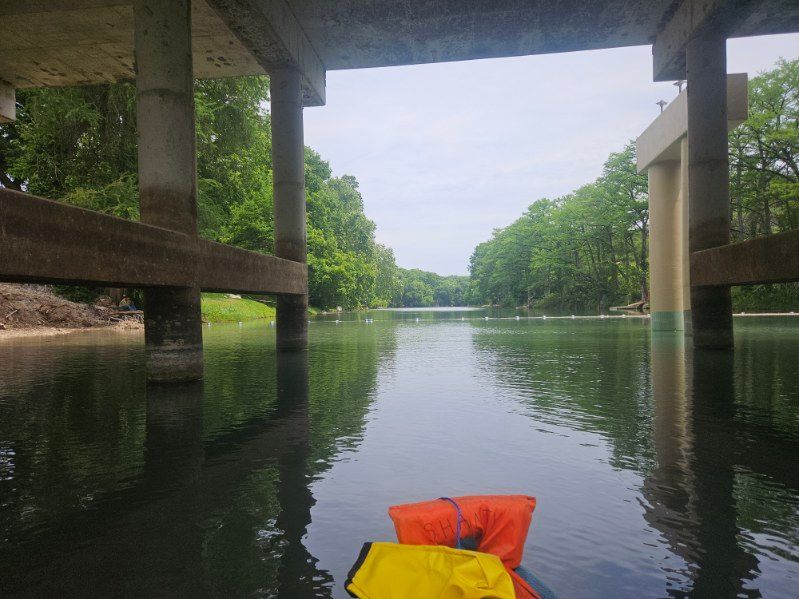 A person in a yellow life jacket is floating on a river under a bridge.
