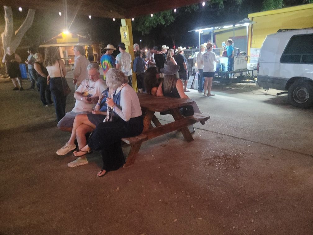 A group of people are sitting at a picnic table in front of a food truck.