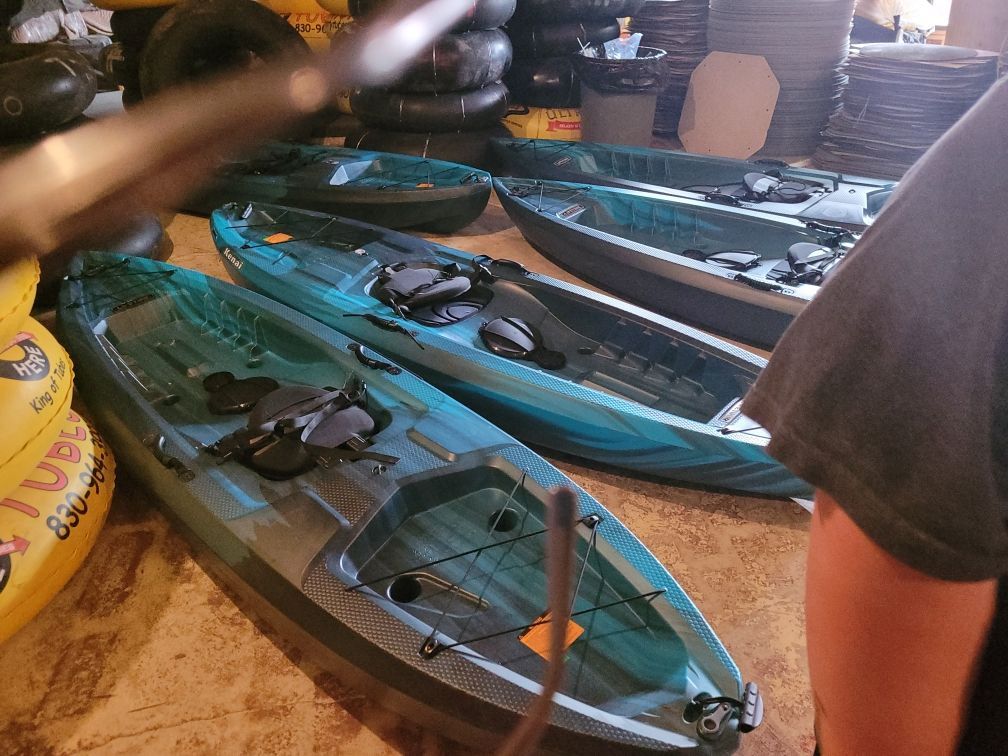 A person is standing in front of a row of kayaks.