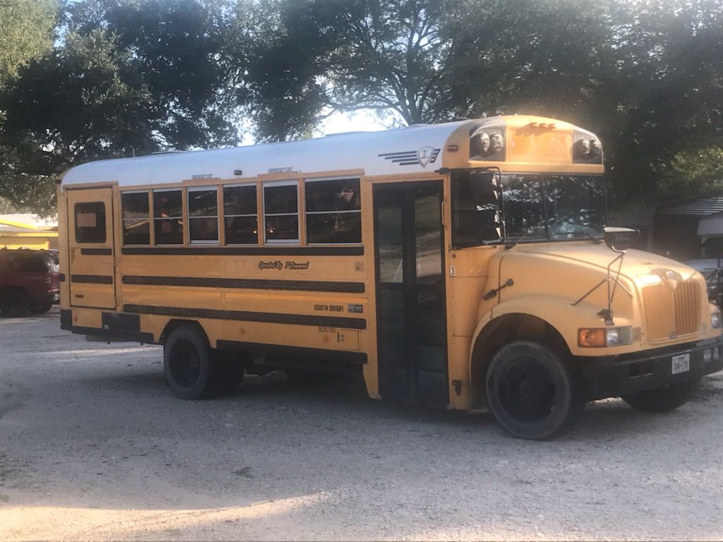 A yellow school bus is parked in a gravel lot.