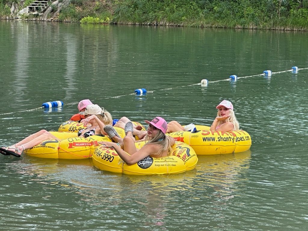 Four people in yellow inner tubes float on a river, wearing hats and enjoying the water.