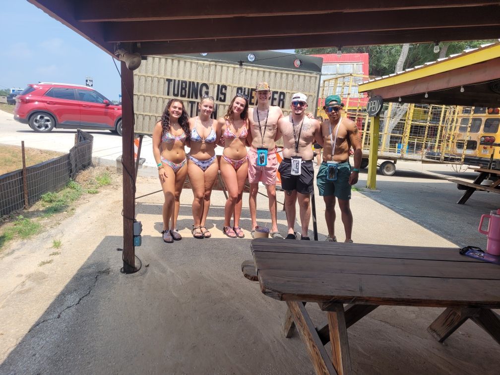 A group of people posing for a picture in front of a sign that says tubing is love