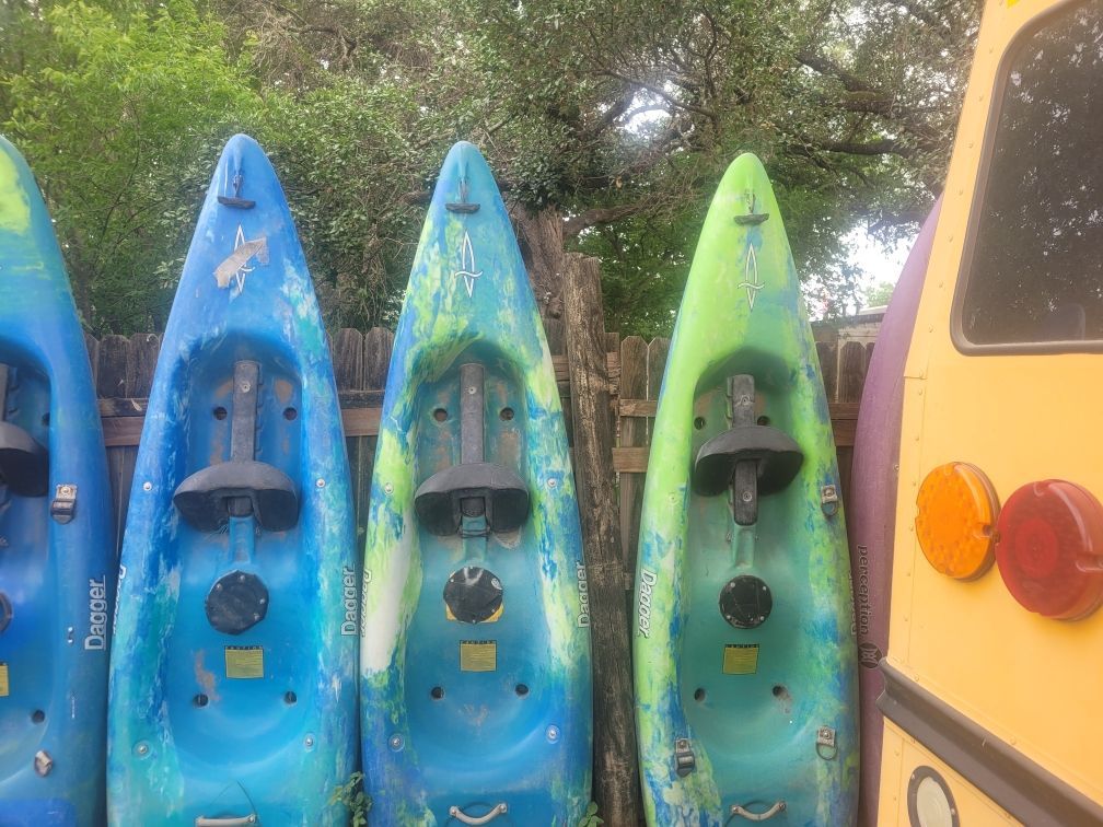 A row of blue and green kayaks are lined up next to a yellow school bus.