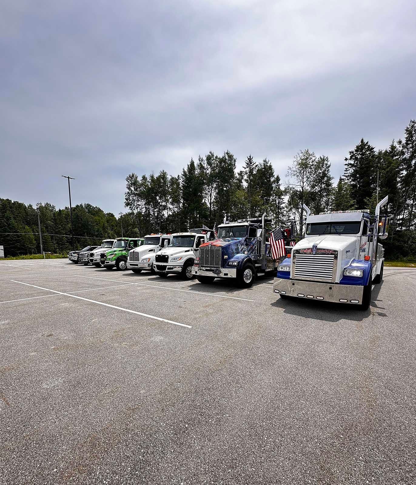 A line of tow trucks parked on gravel in a lot