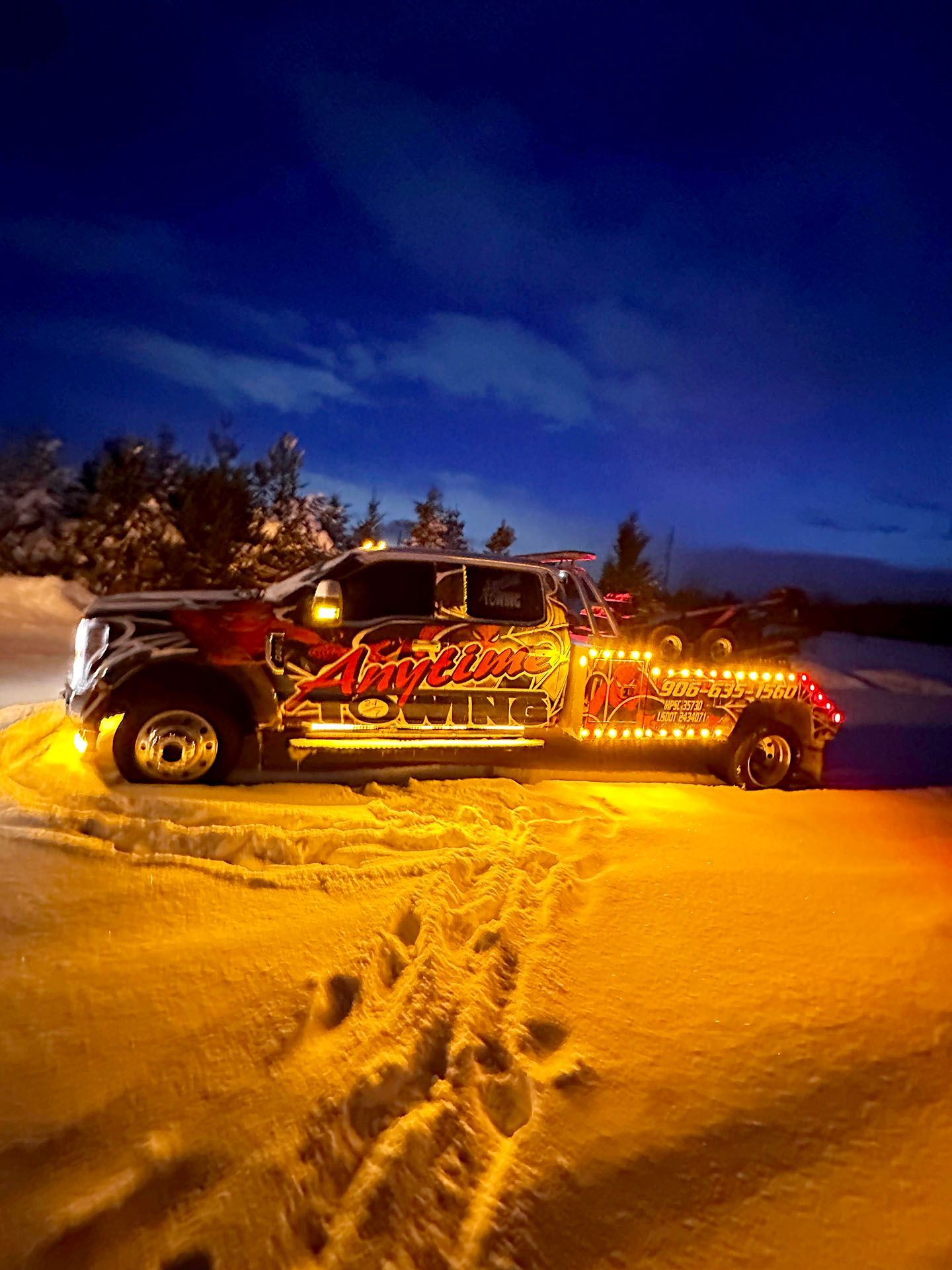 Tow truck covered in lights on a snowy road at night