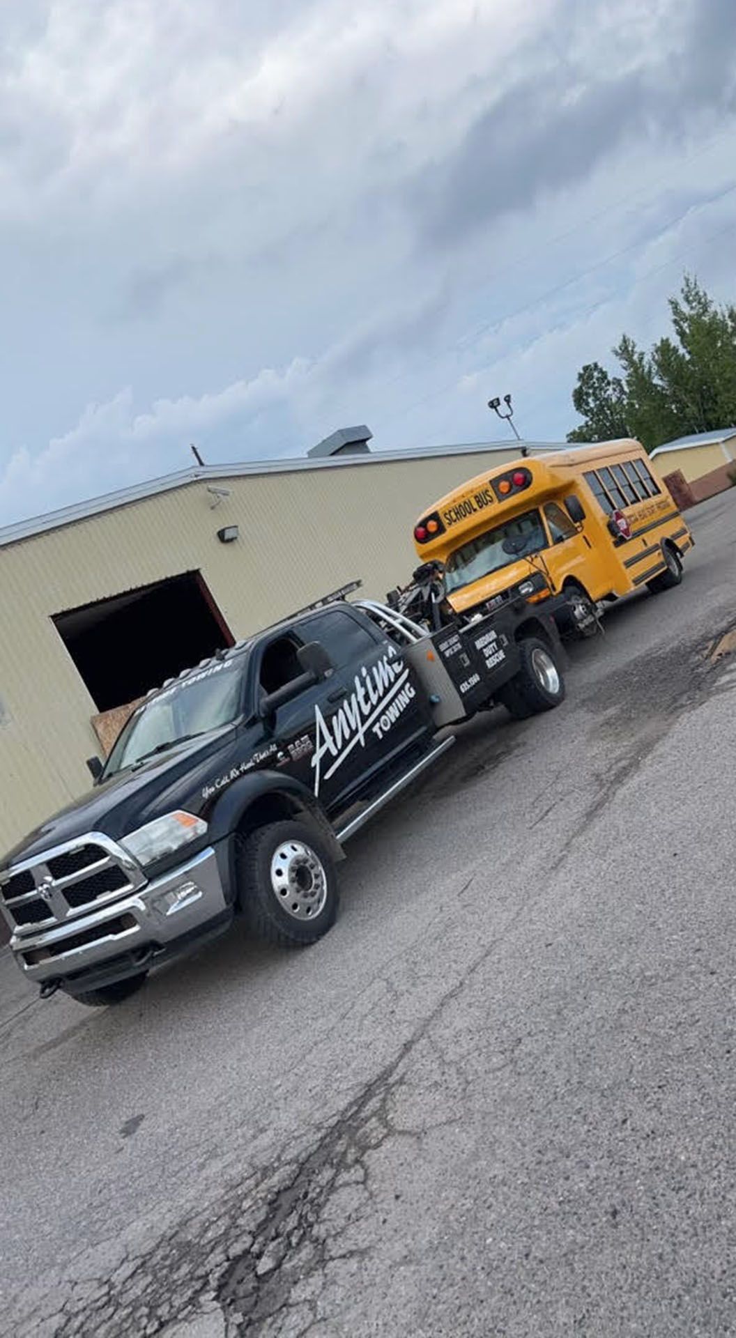 Black tow truck towing a small yellow school bus on an asphalt road