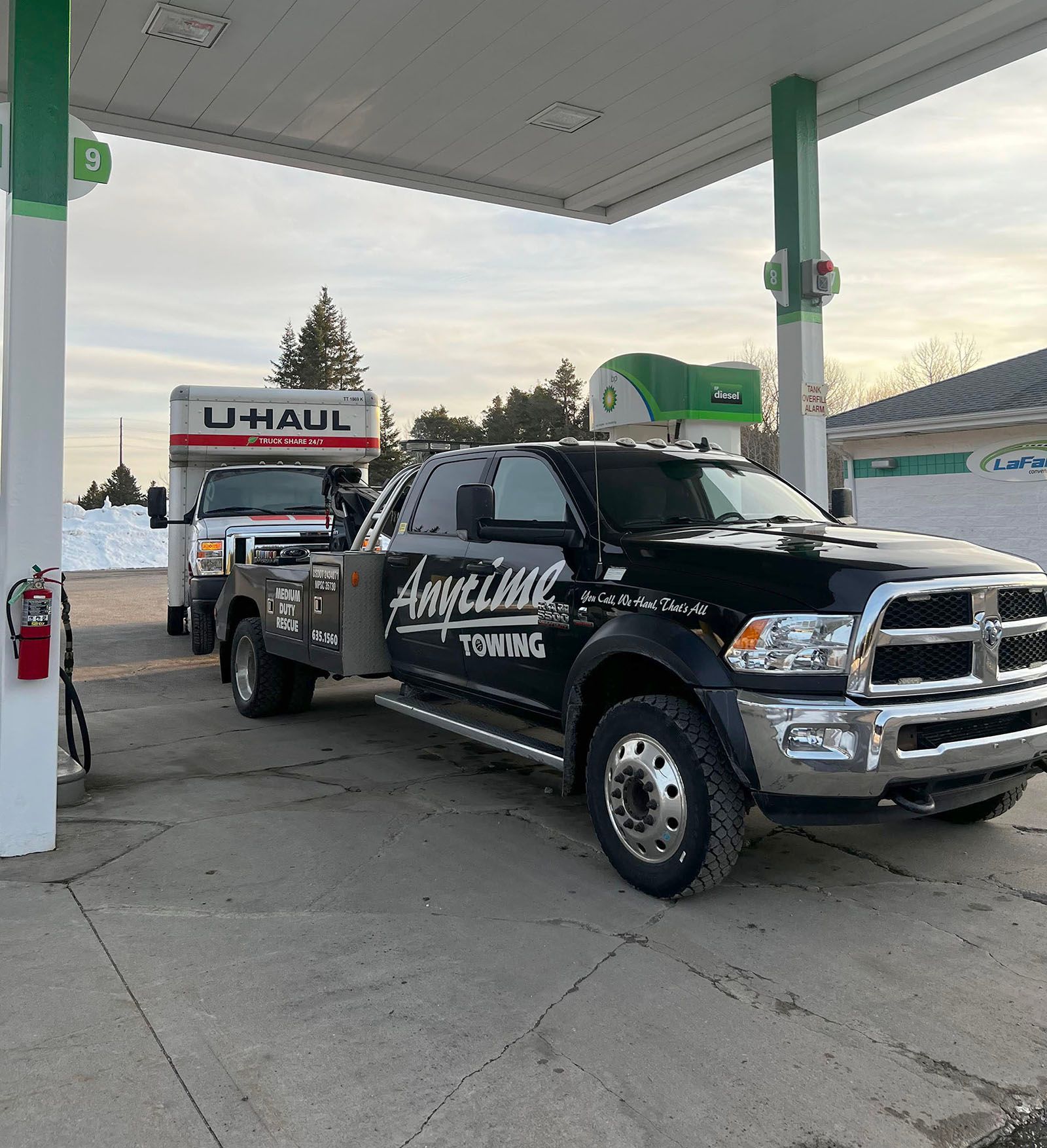 Black tow truck towing a U-Haul trailer at a gas station