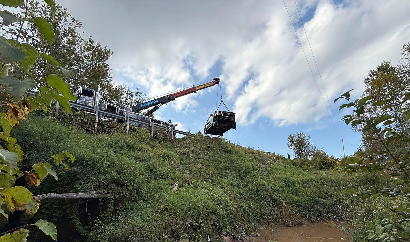 A crane lifting a dark vehicle from a grassy slope