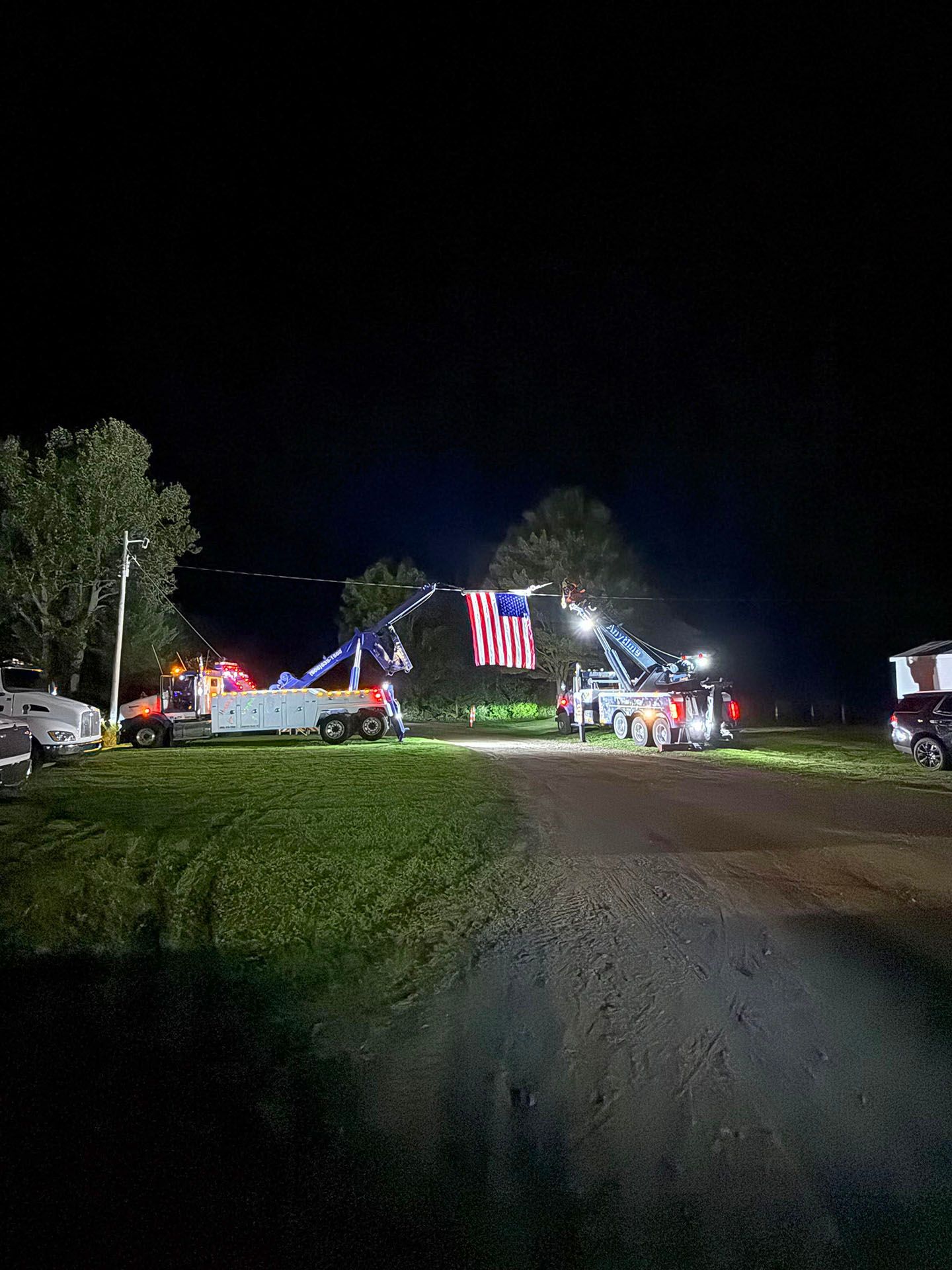 Two tow trucks with American flag suspended at night